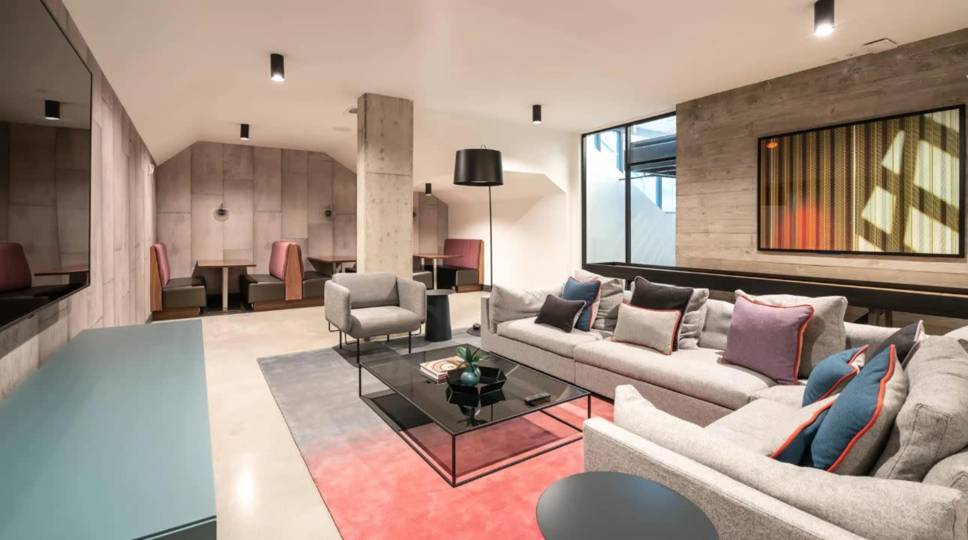 A modern living room featuring a gray sectional sofa, a glass coffee table, and large windows with a view of a dining area in the background.