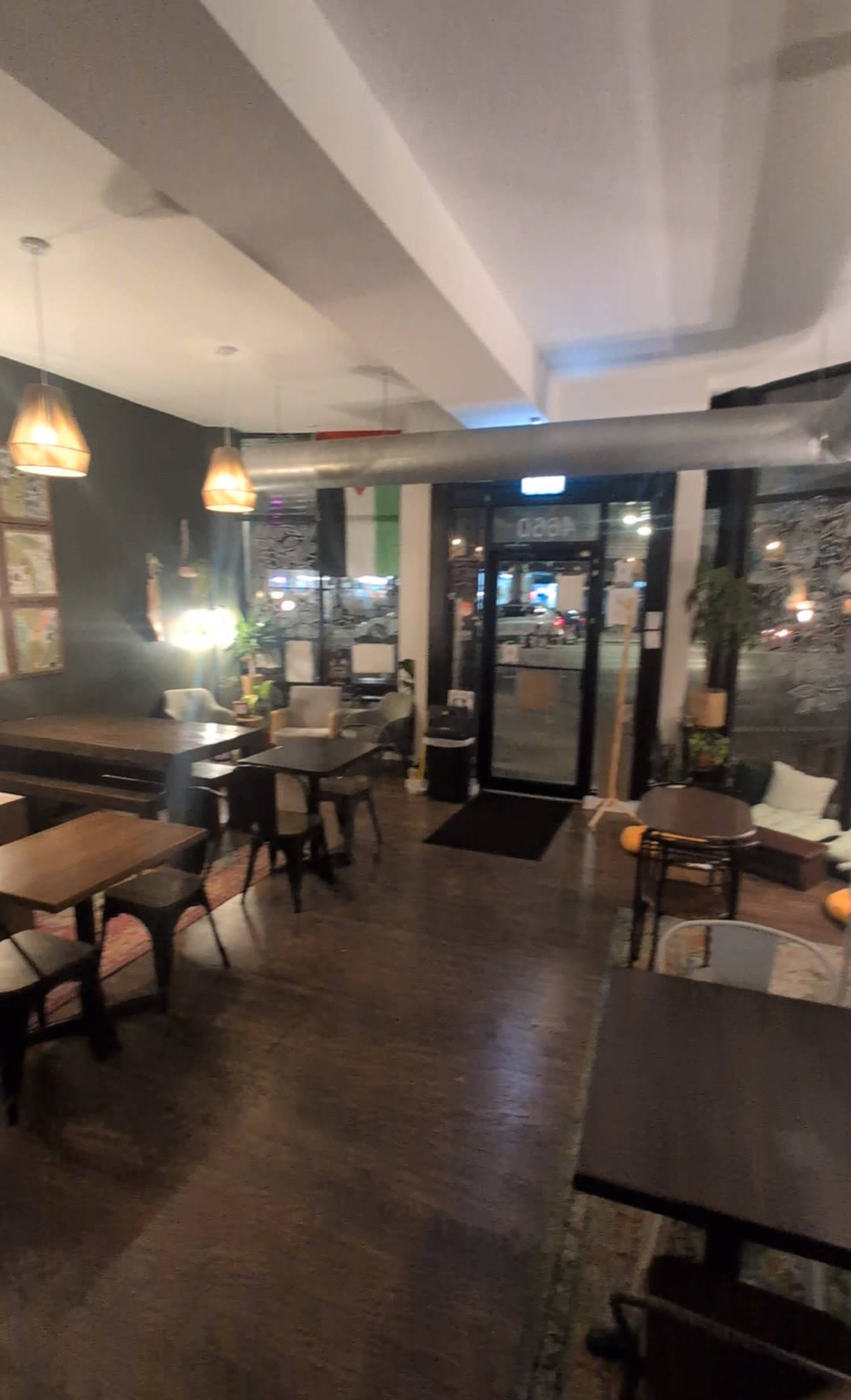 The image shows a cozy café interior with wooden tables, chairs, and decorative lamps, illuminated by light coming from the entrance.