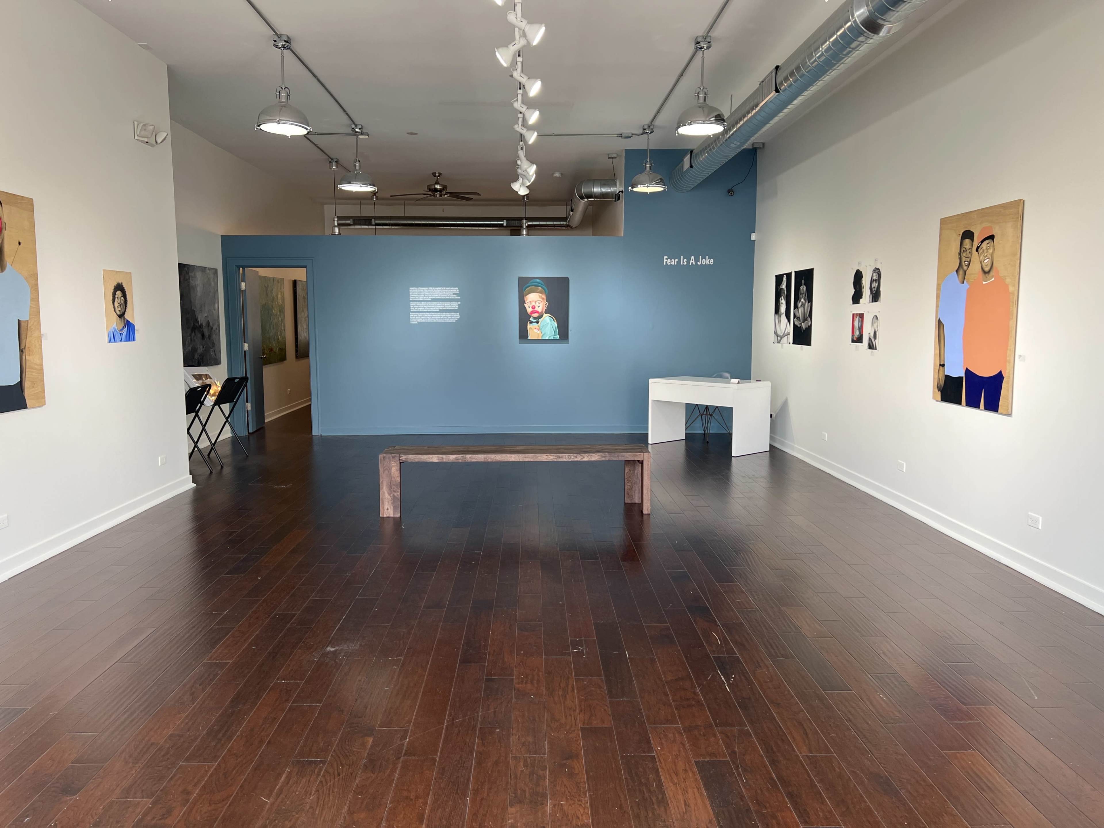 A spacious art gallery with wooden flooring, featuring several framed paintings on the walls and a bench in the center of the room.