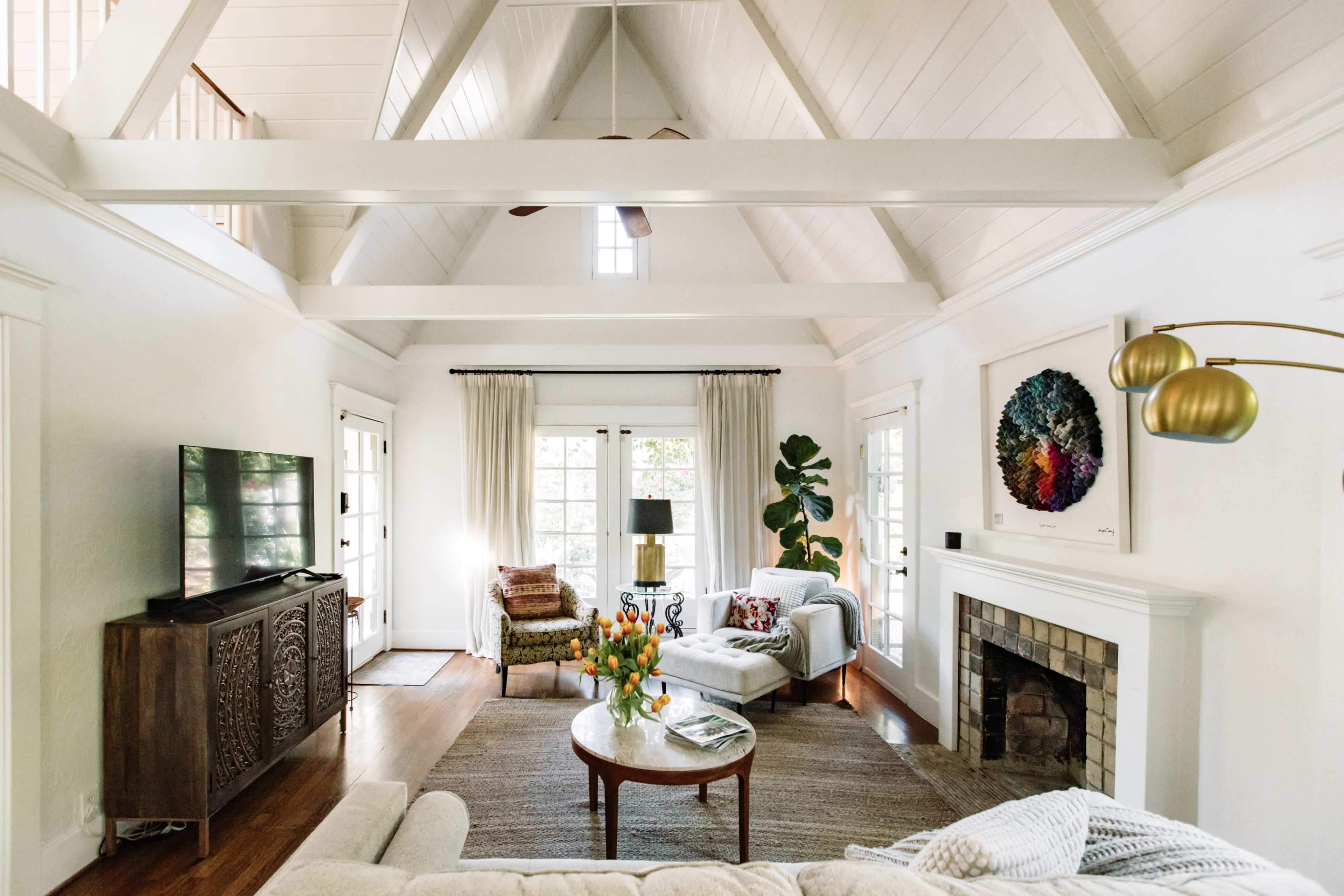 A spacious living room with a high, vaulted ceiling, featuring a comfortable seating area, a coffee table, and large windows that provide natural light.