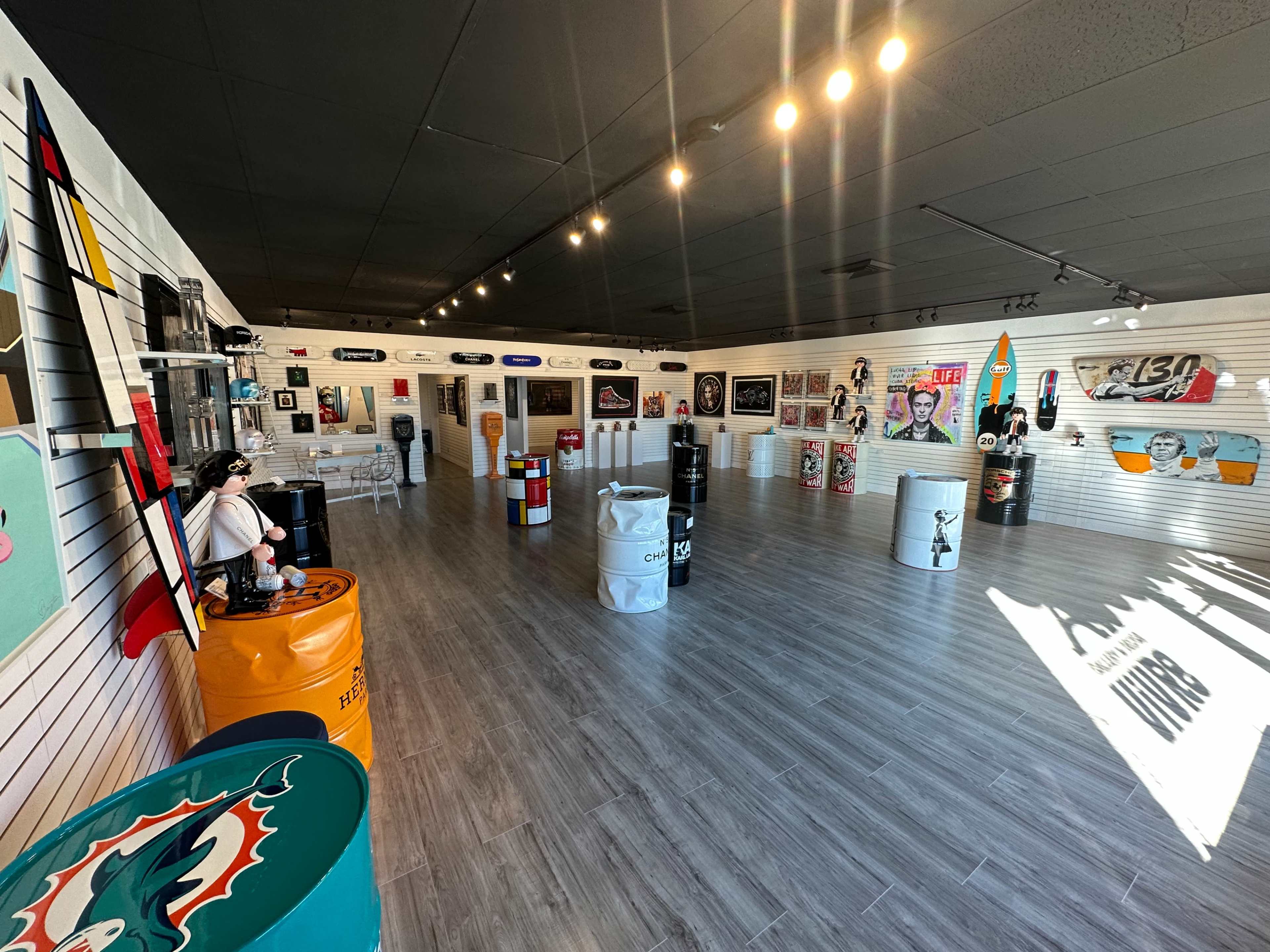 An art gallery featuring colorful barrels and various artworks displayed on the walls.