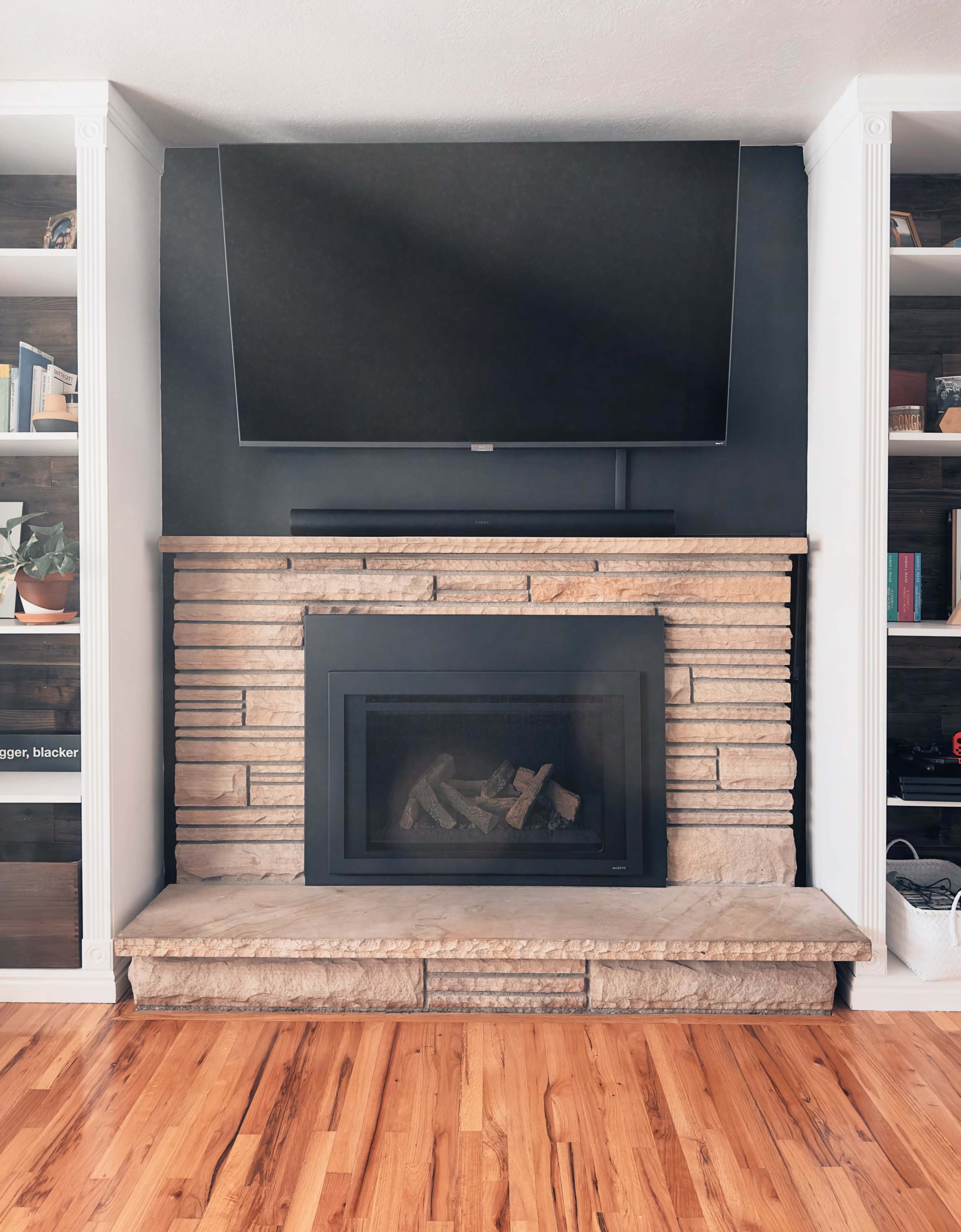 A modern fireplace with a stone surround, beneath a wall-mounted television in a room featuring wooden flooring and built-in shelves.