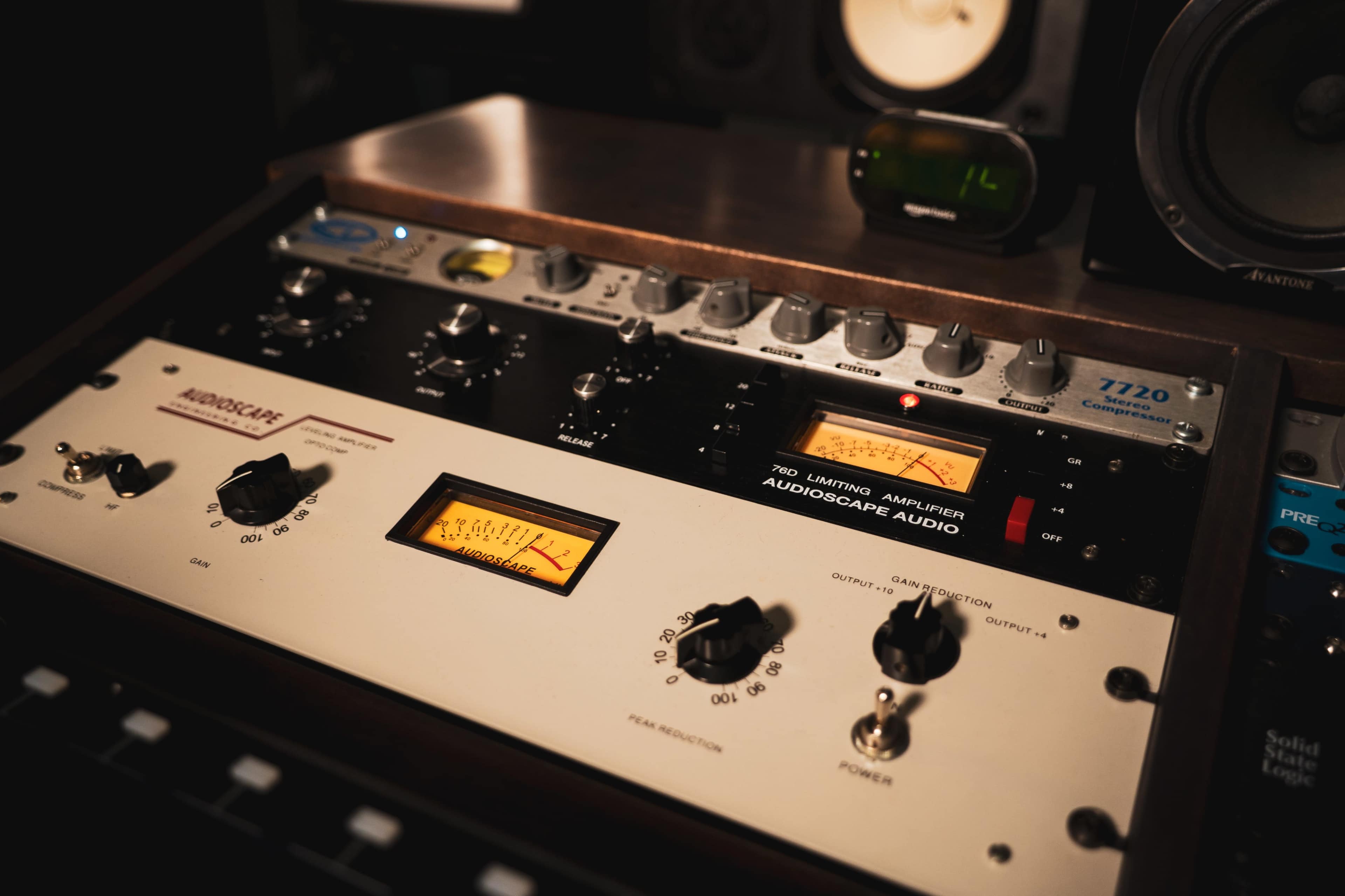 The image shows a close-up of audio equipment featuring knobs, dials, and analog meters.