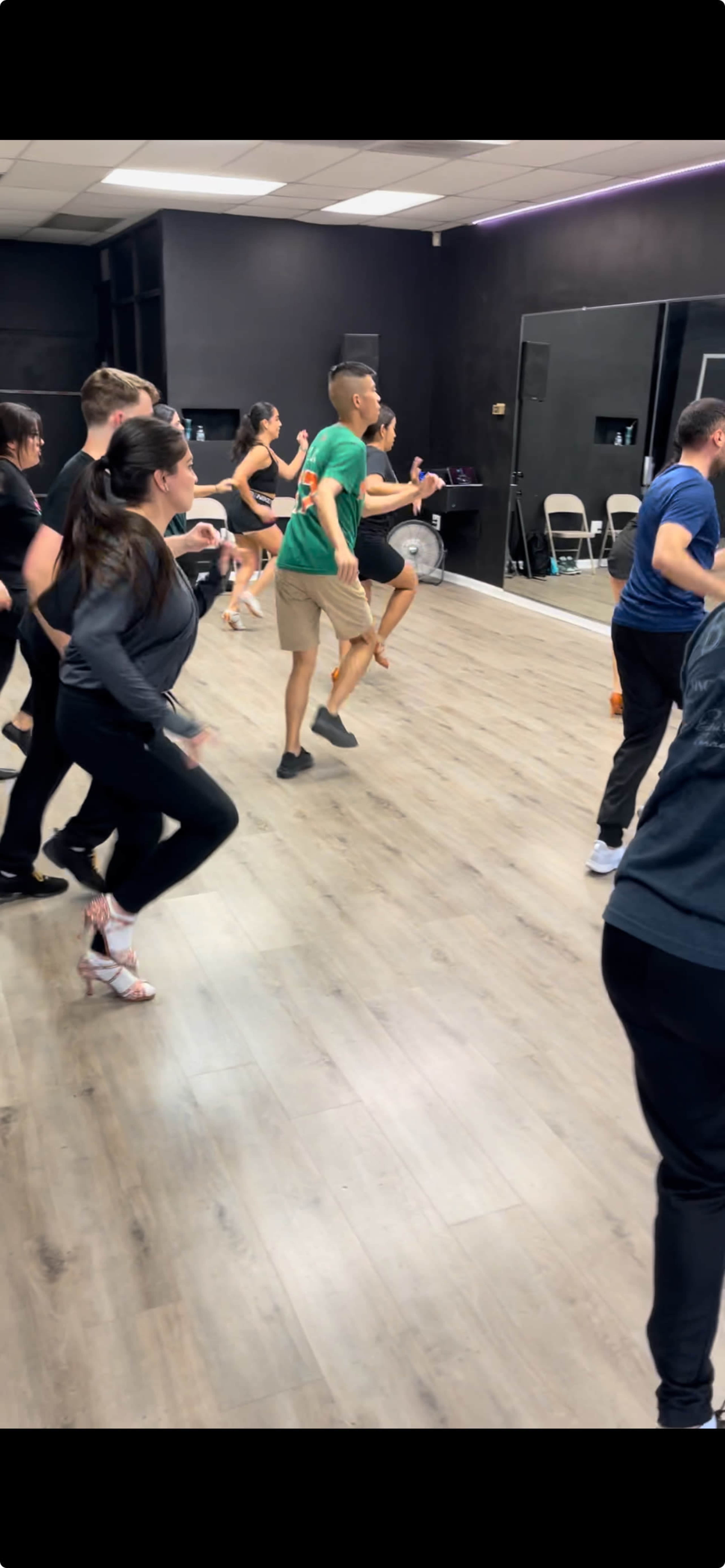 A group of people is participating in a dance class in a studio with a mirror.