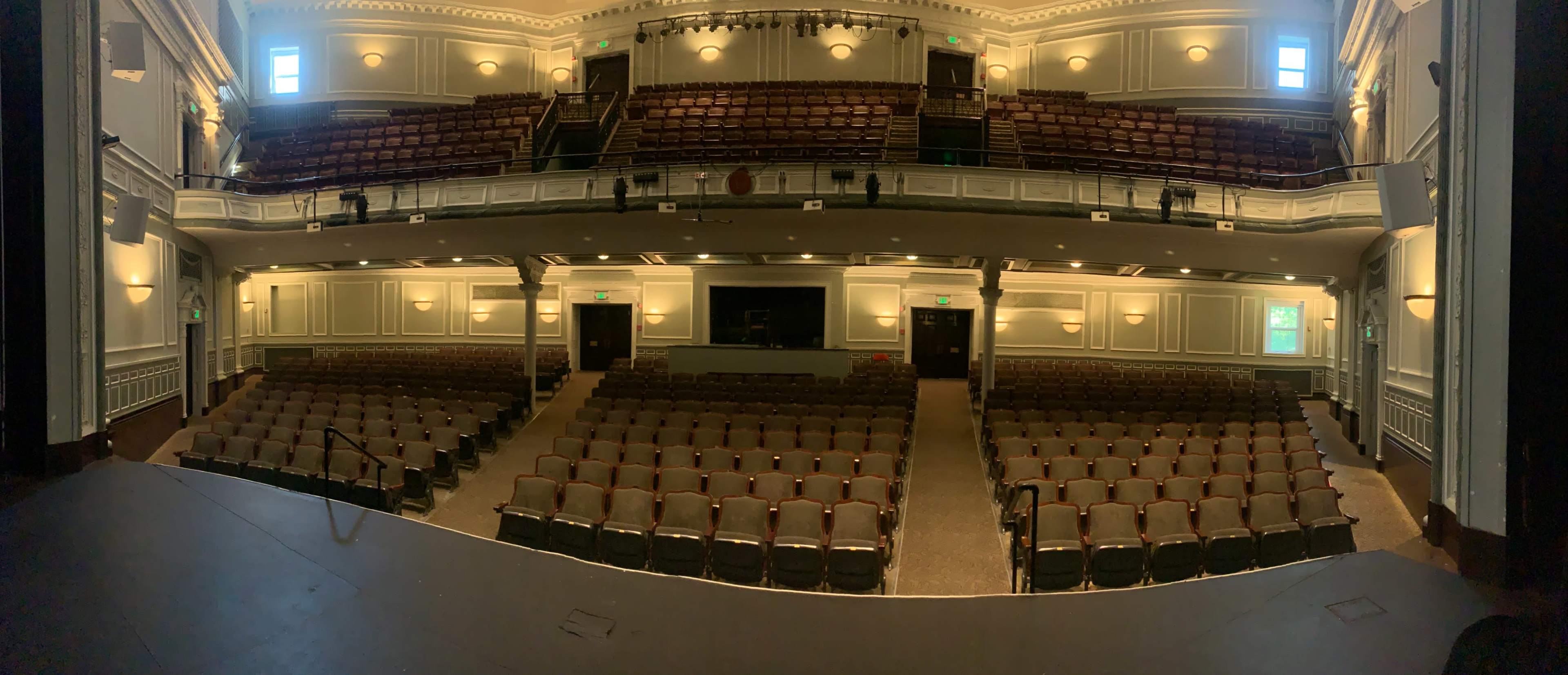 The image shows a nearly empty theater with rows of seats arranged in a semicircle, viewed from the stage.