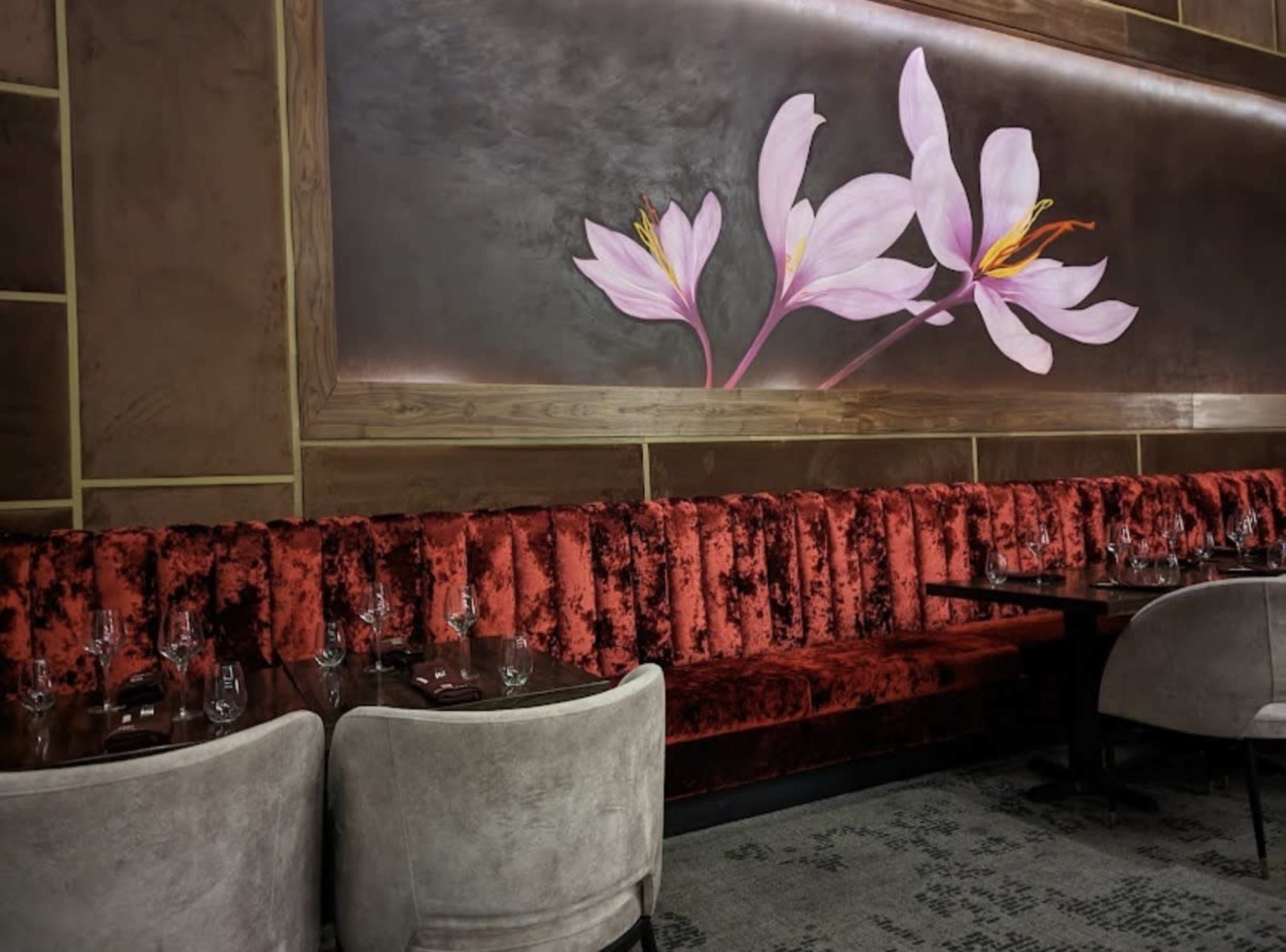 The image shows a restaurant interior featuring a red velvet banquette with a floral mural on the wall above.
