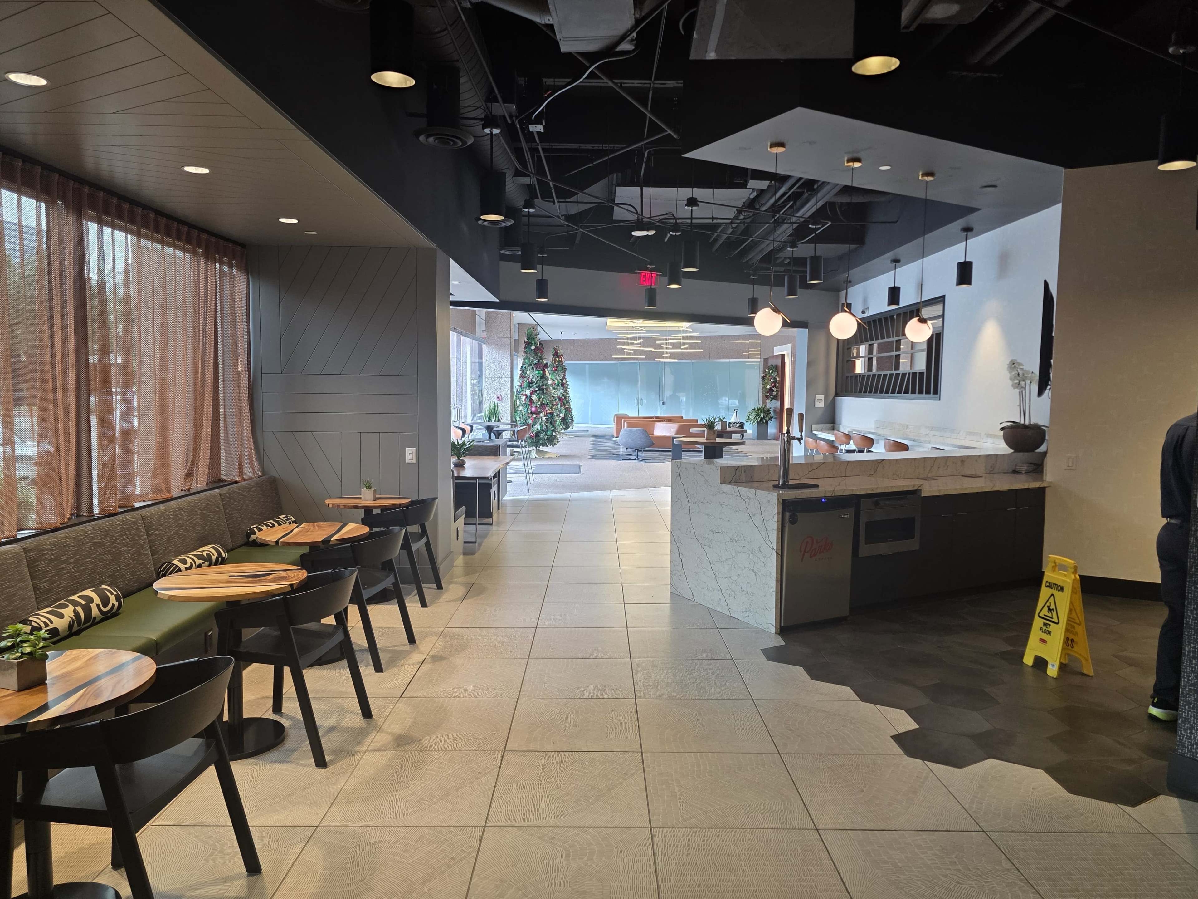 The image shows a modern indoor space of a restaurant or café featuring seating areas, a counter, and a view of a decorated Christmas tree in a distant lounge area.
