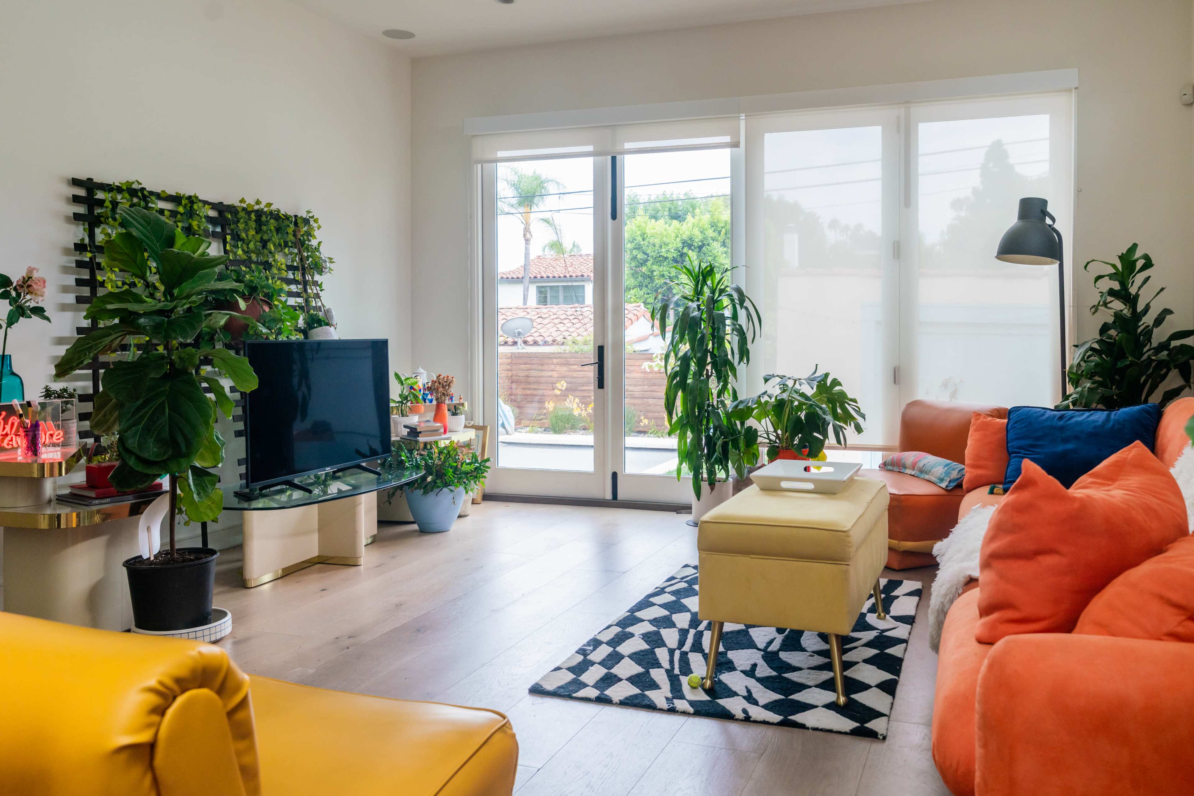The image shows a bright living room featuring a large window, a television, and comfortable seating arranged around a coffee table.