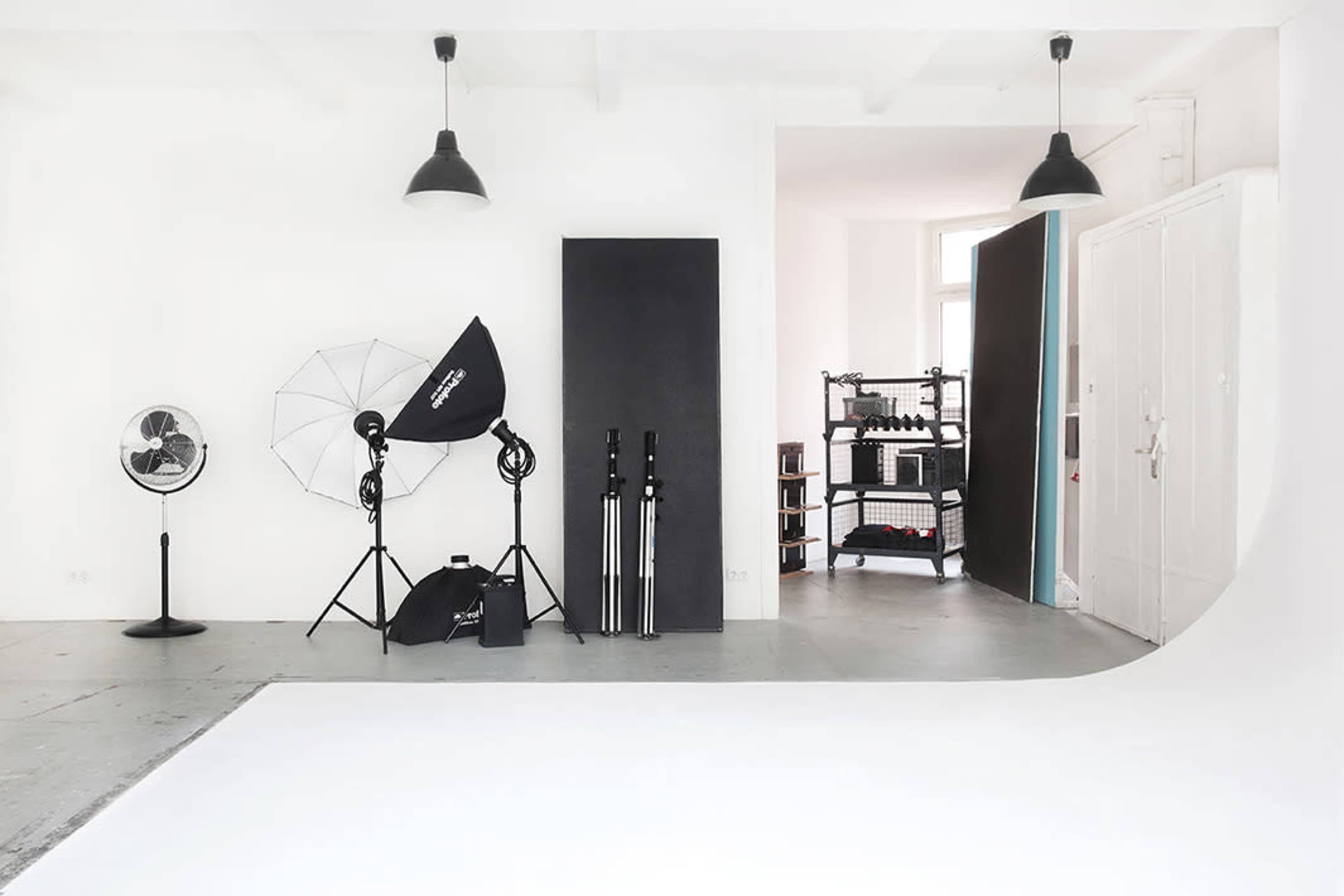 A minimalistic photography studio featuring a backdrop, lighting equipment, a fan, and storage for props.