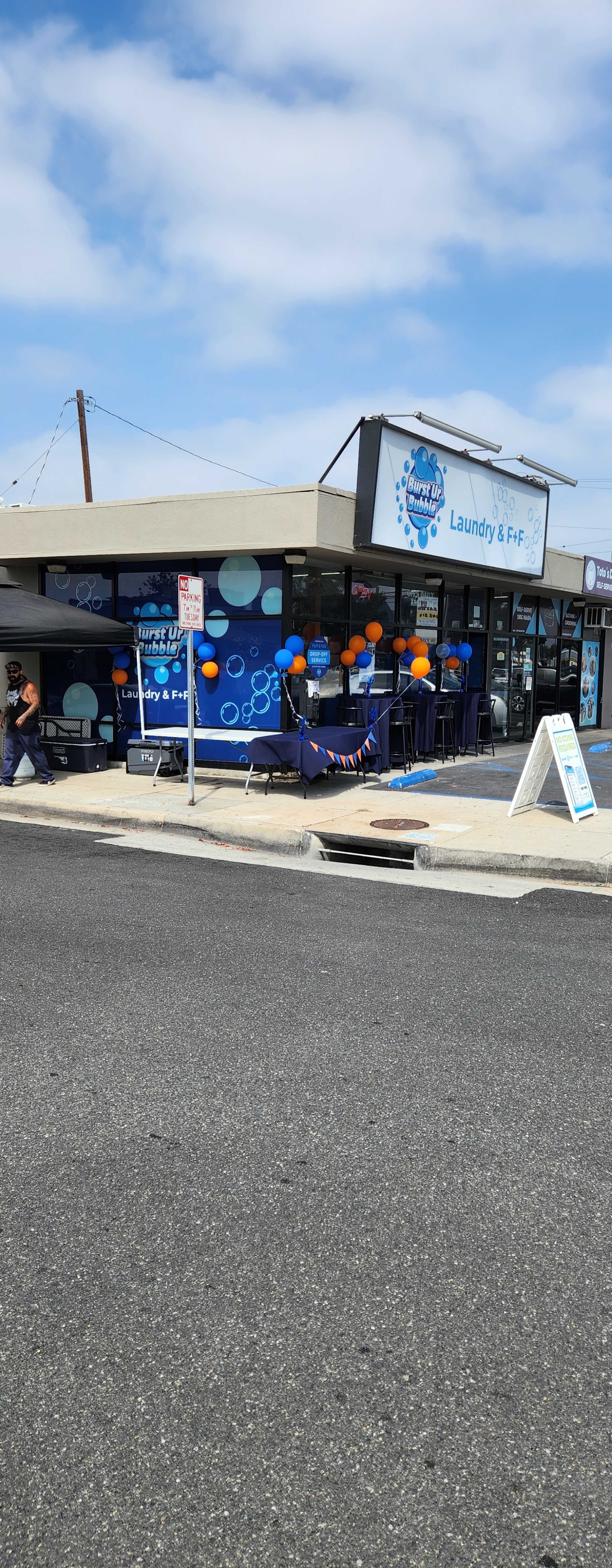 A laundry service storefront features a blue and white sign, outdoor seating with orange balloons, and a sidewalk menu display.