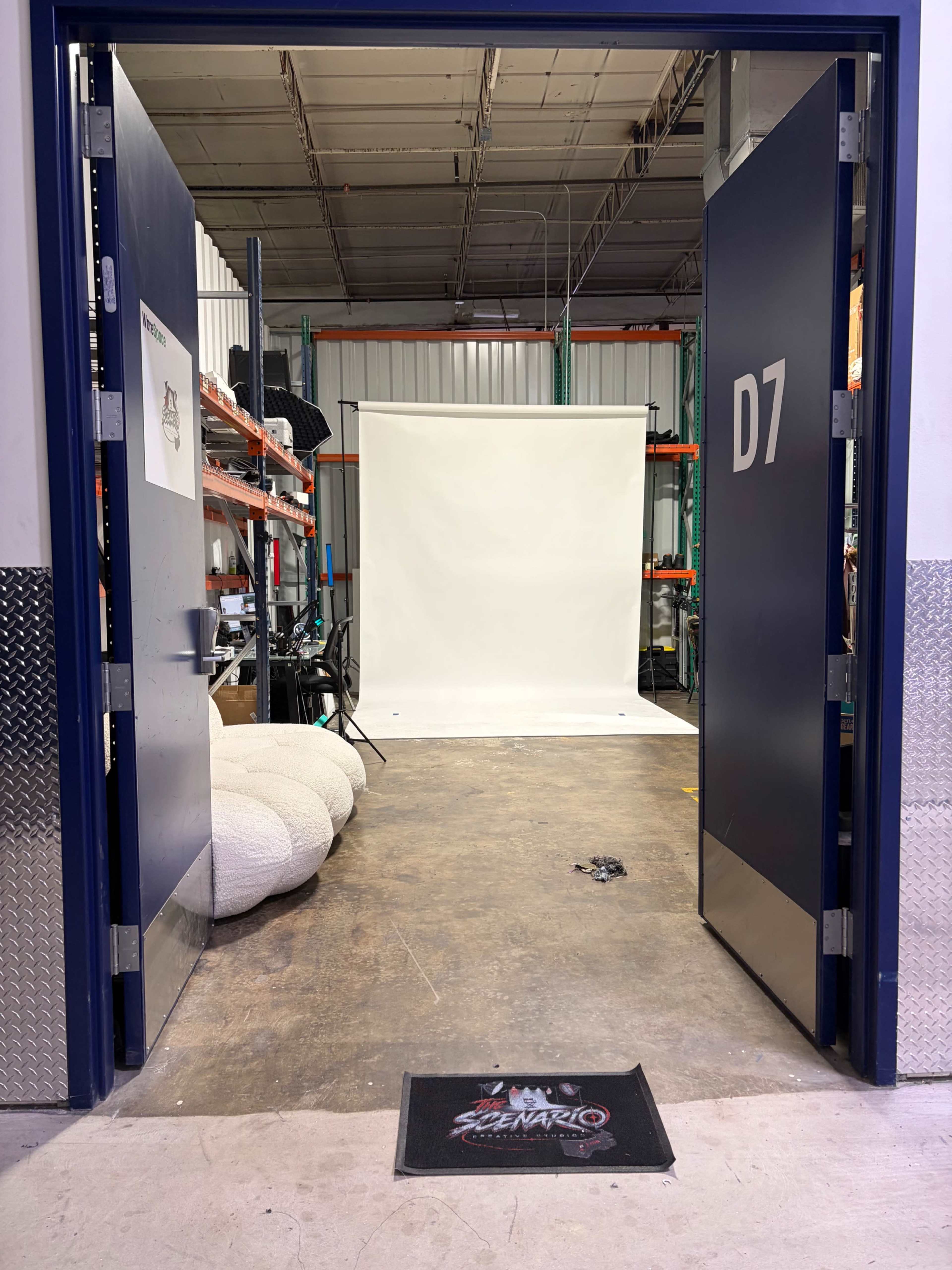 The image shows an open warehouse door leading to a studio space with a white backdrop and equipment visible in the background.