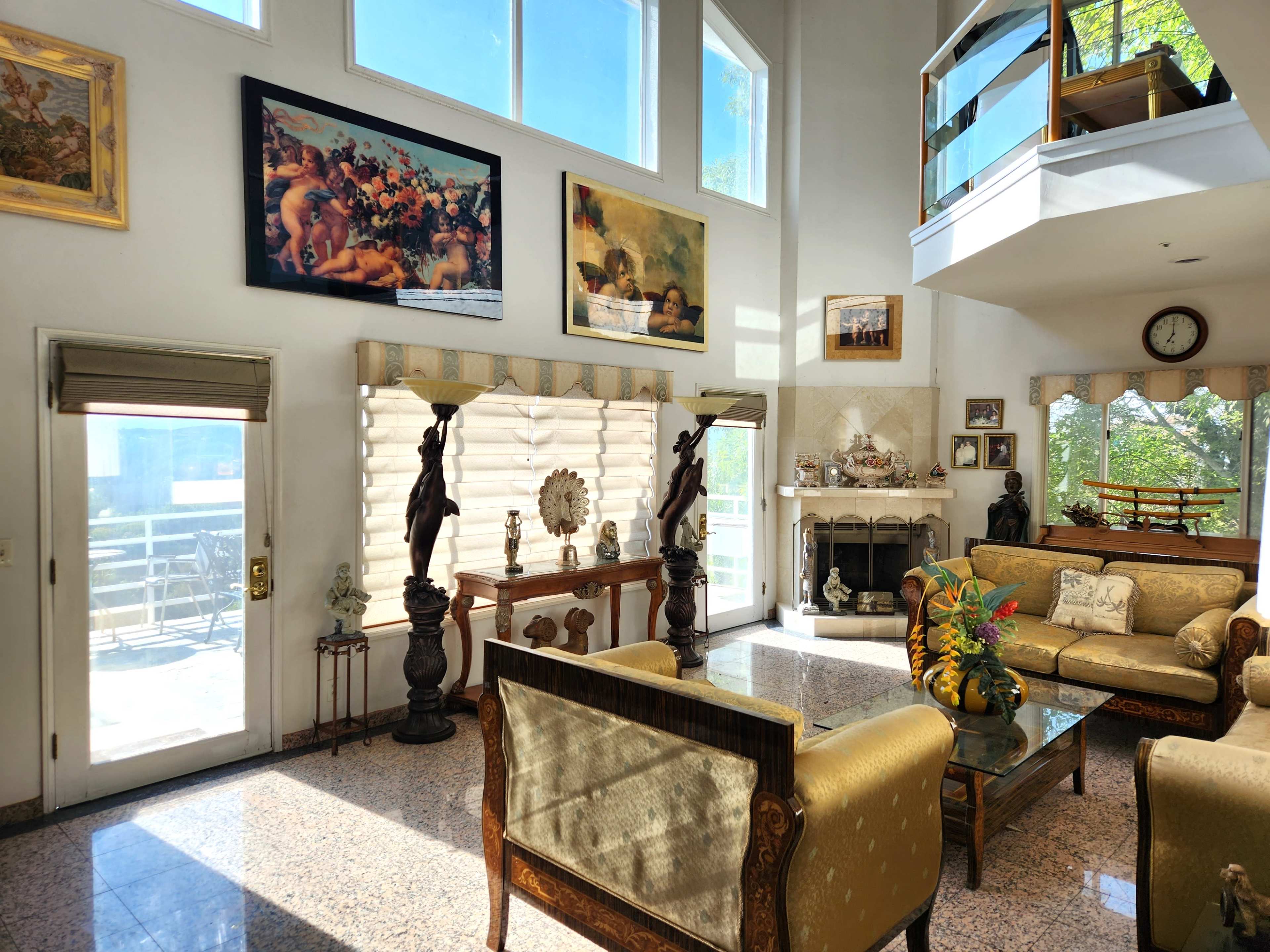 The living room features a high ceiling, large windows, and a mix of decorative art, with seating arrangements centered around a coffee table.