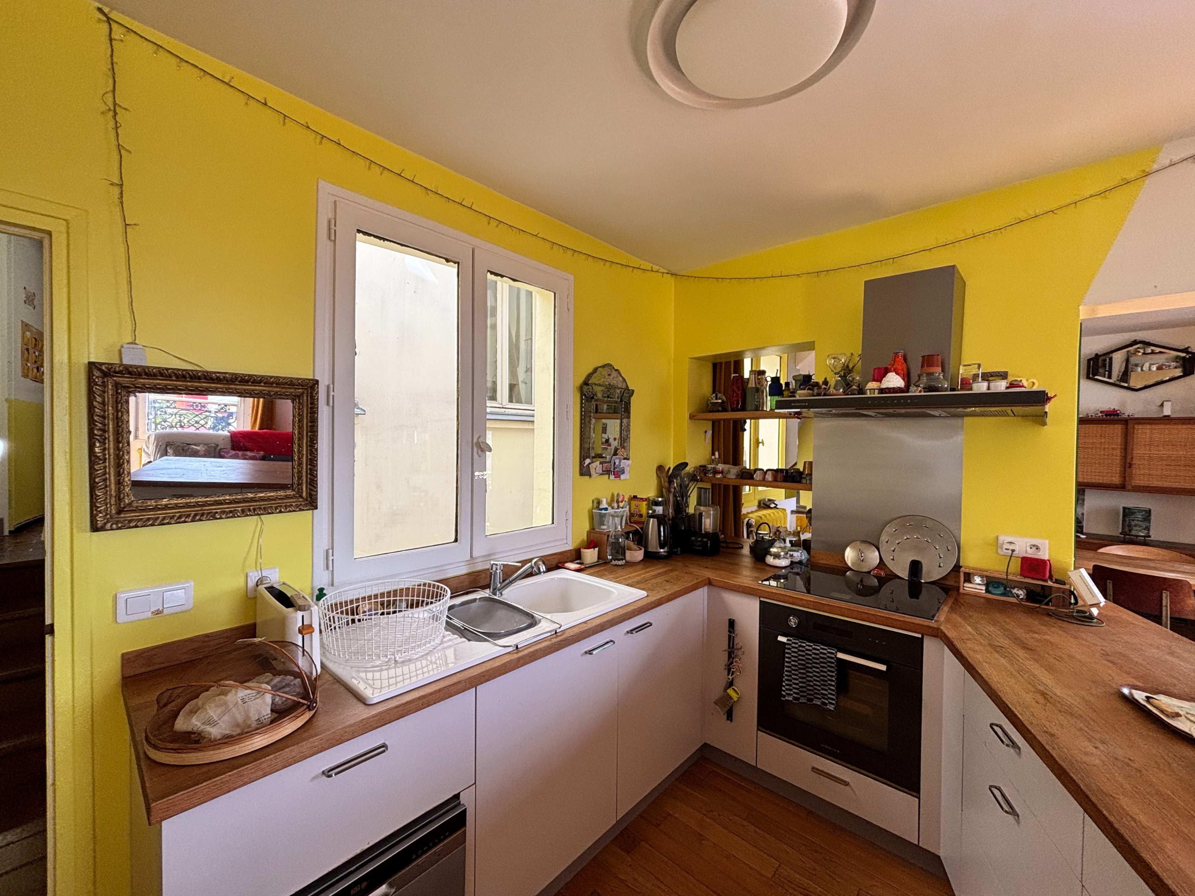 The image shows a kitchen with yellow walls, a wooden countertop, and various appliances and utensils arranged on the shelves.