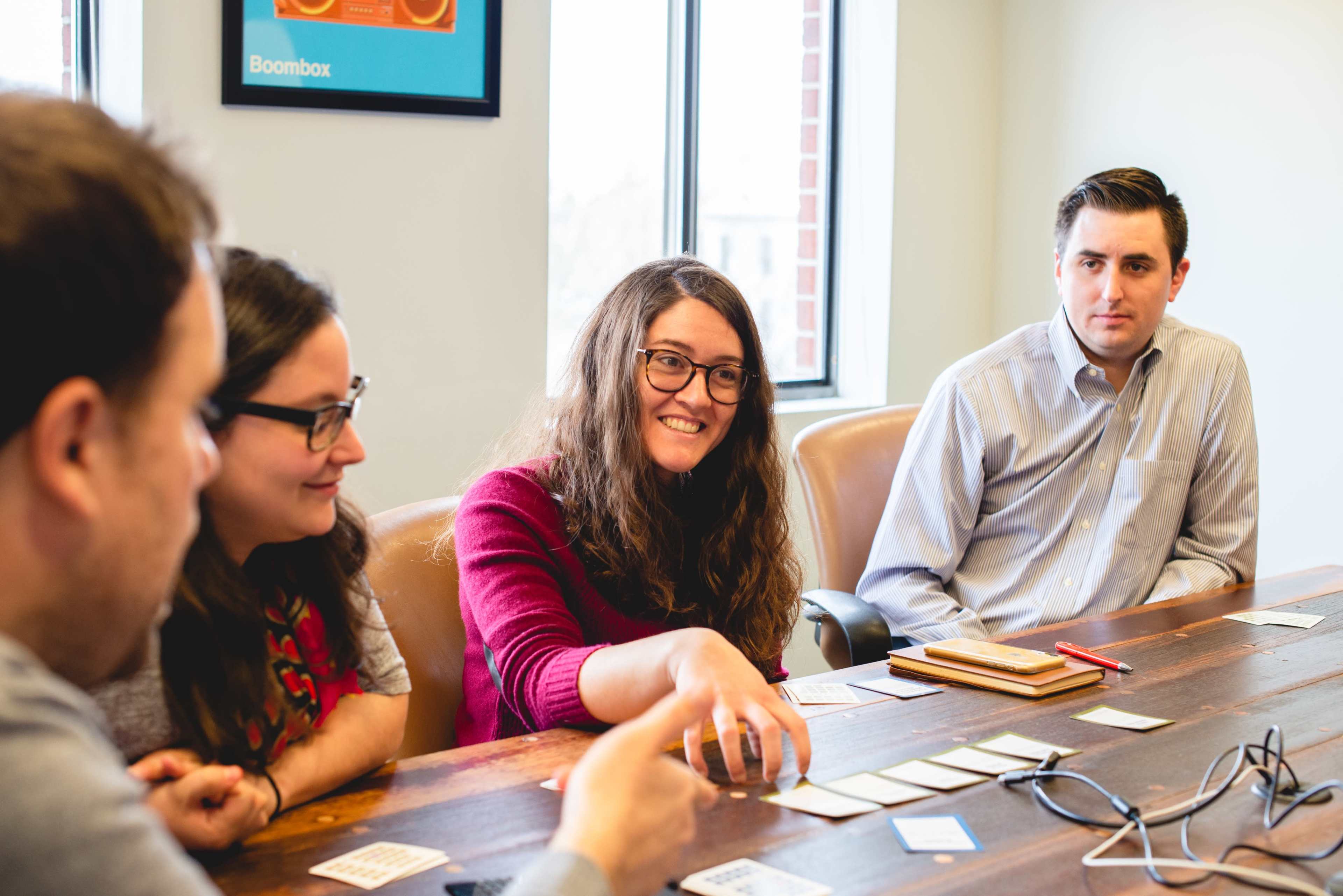 A group of four people sits around a wooden table, engaged in a discussion with cards laid out in front of them.