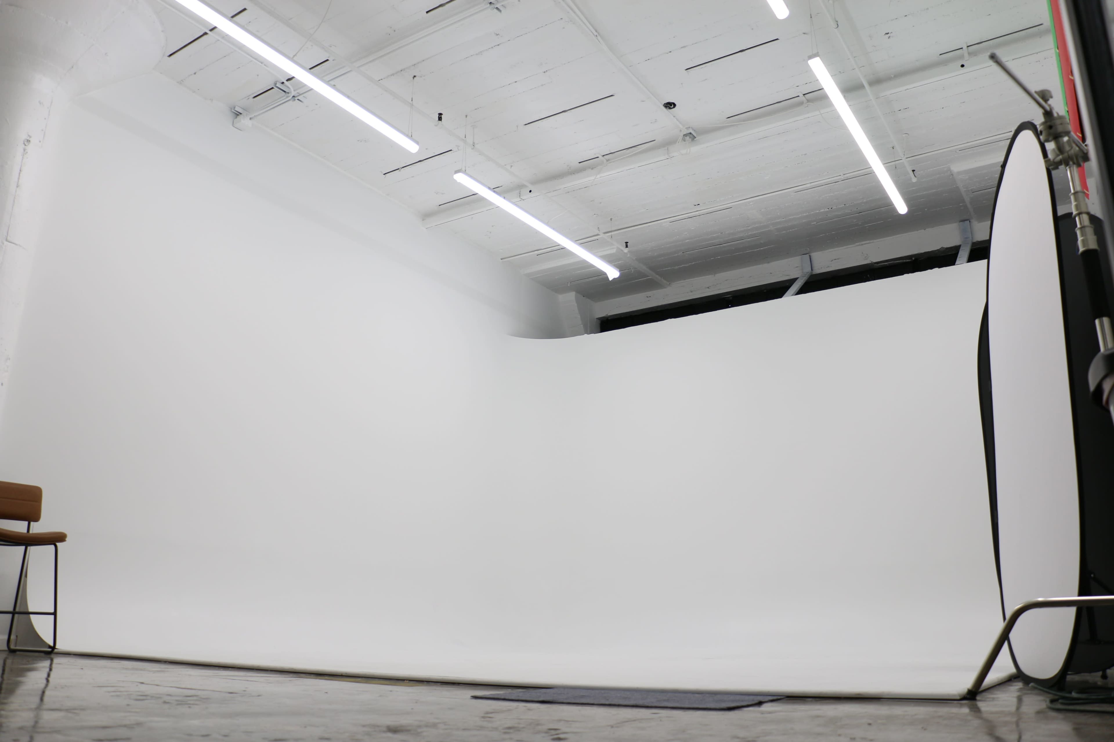 The image shows a spacious photography studio with a seamless white backdrop and minimal furnishings.
