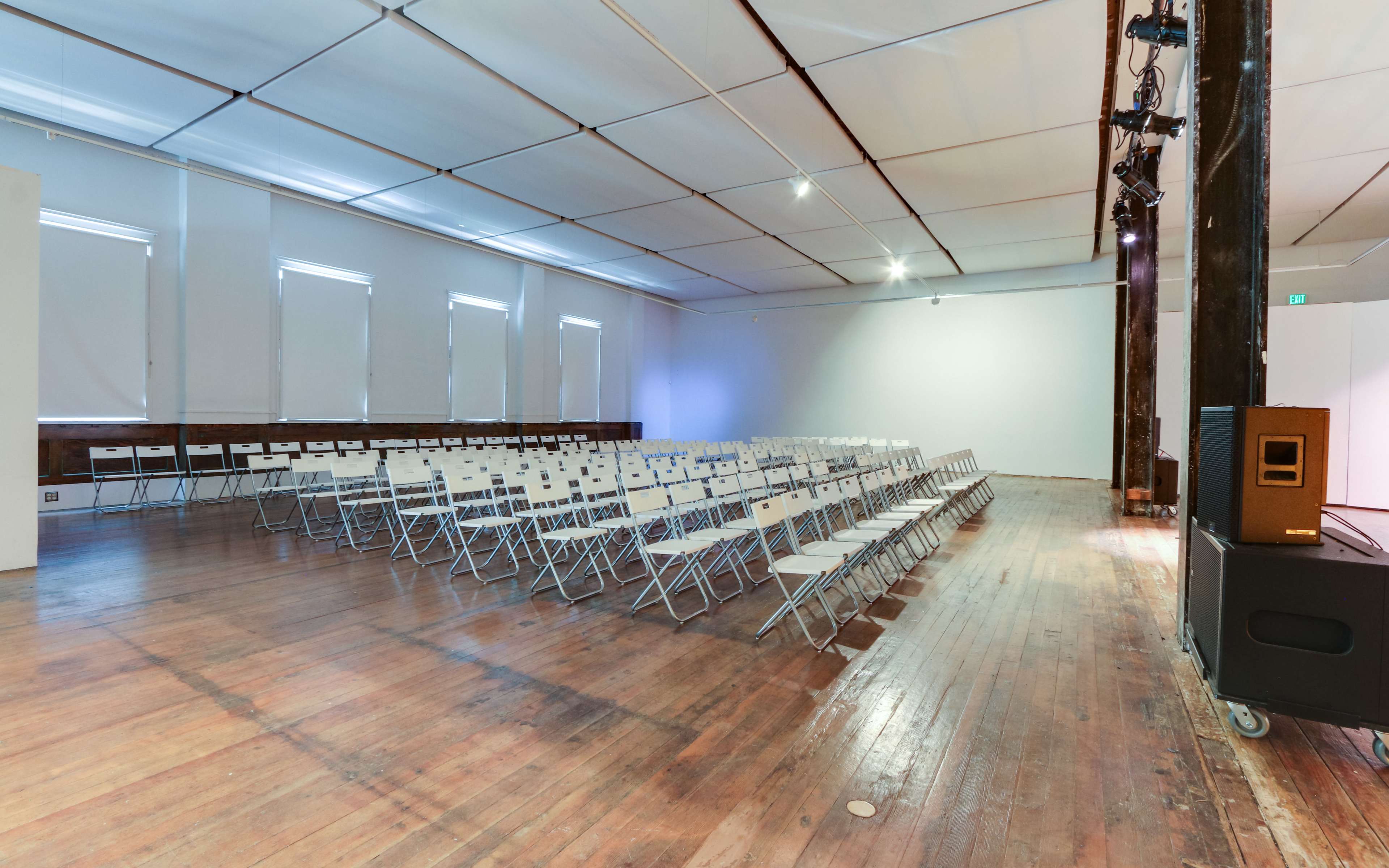 A spacious room with wooden flooring is set up with rows of empty folding chairs facing a blank wall.