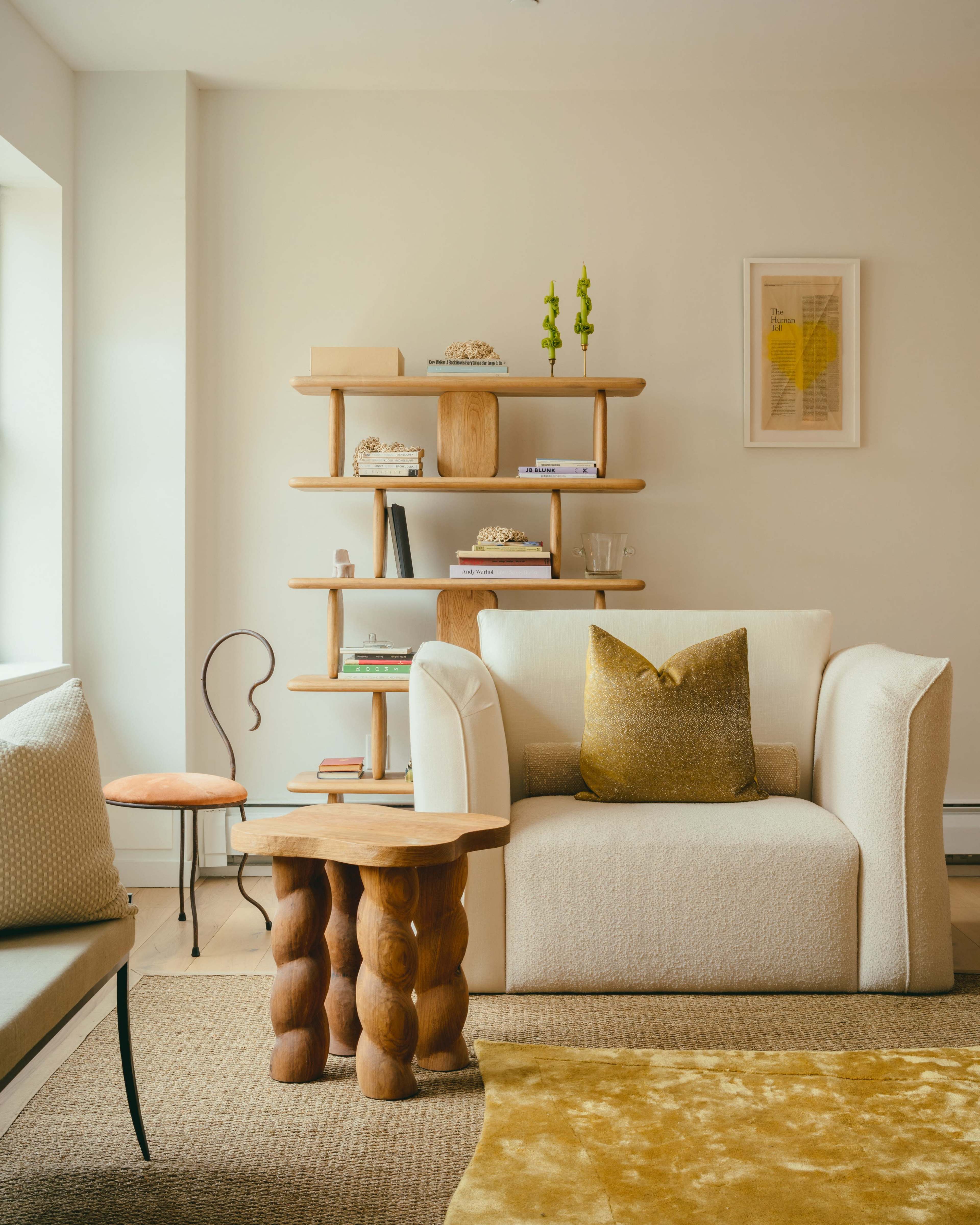A modern living room setting with a cream-colored sofa, a textured coffee table, and a wooden bookshelf displaying various decorative items.