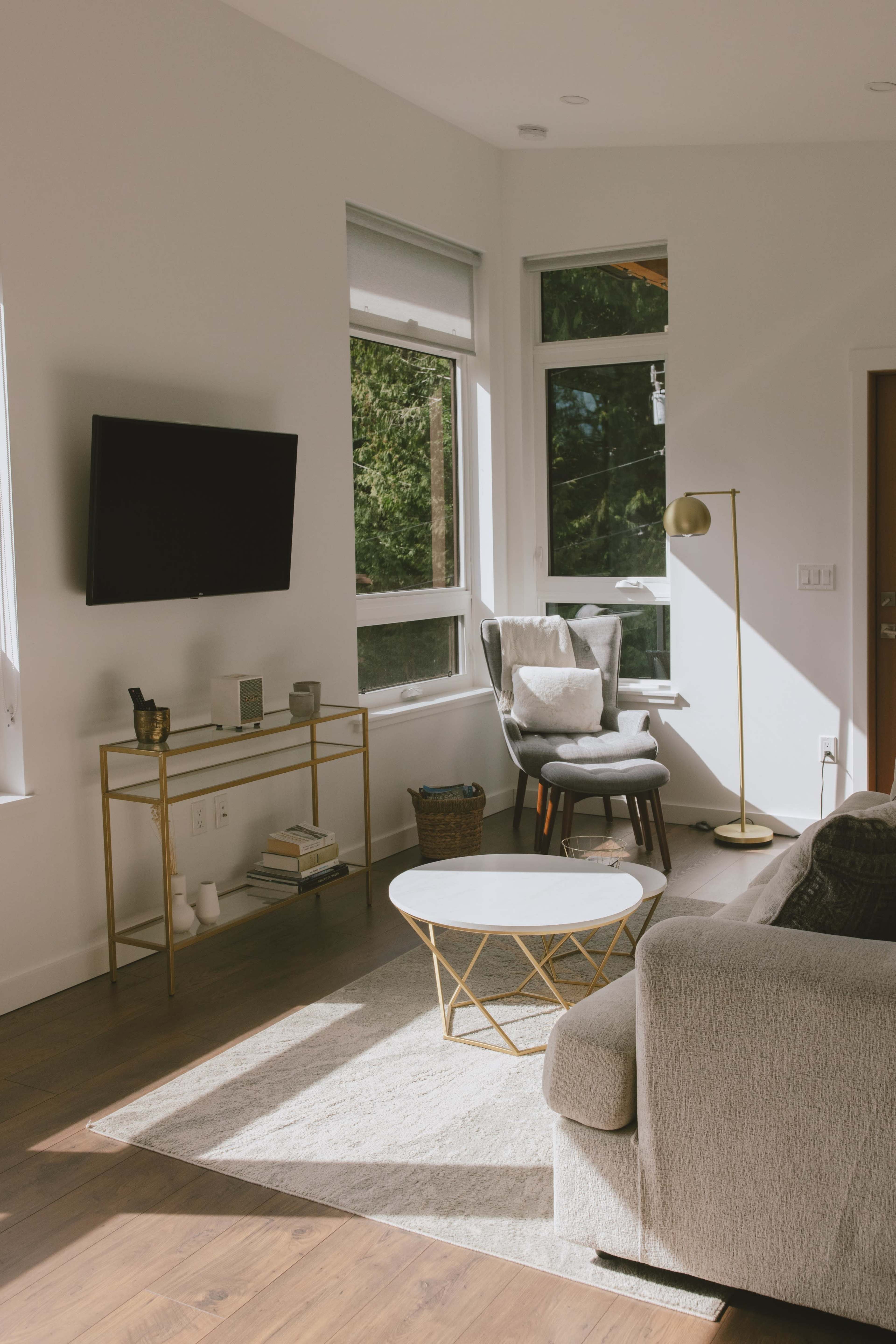 A modern living room with a gray sofa, a round coffee table, a gold floor lamp, and large windows allowing natural light to enter.