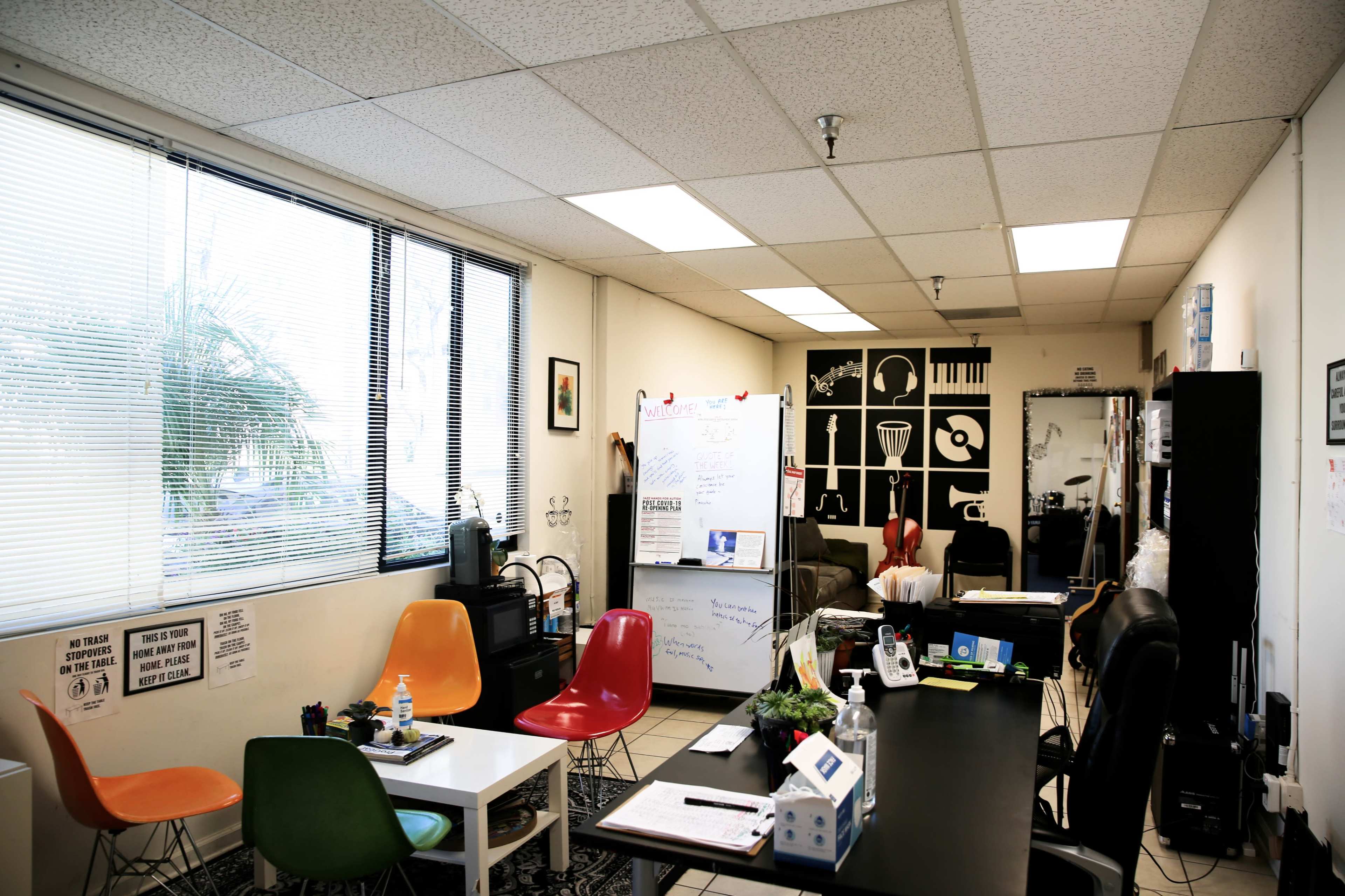 A modern office space features colorful chairs, a large whiteboard, and wall art depicting musical instruments.