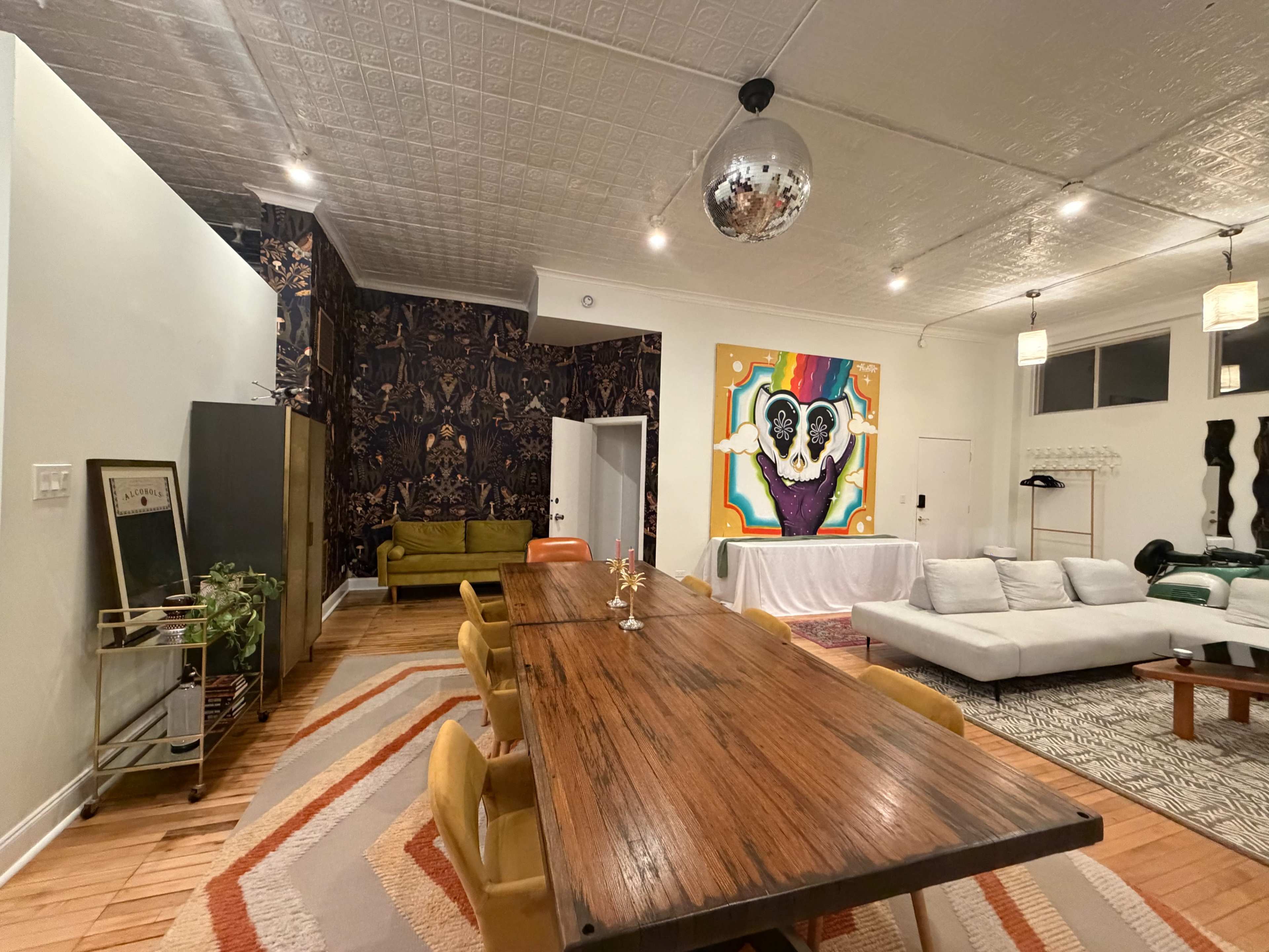 The image shows a modern interior space with a dining table, a seating area, and vibrant artwork on the walls.