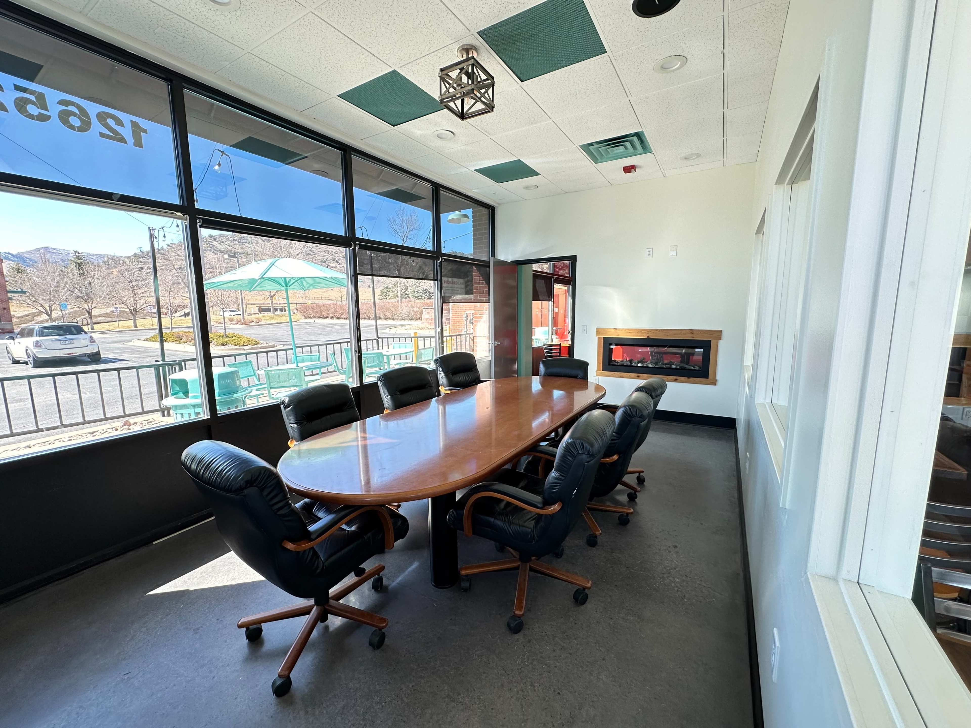 A large conference room features a wooden table surrounded by eight black ergonomic chairs, with windows offering a view of the outdoors.