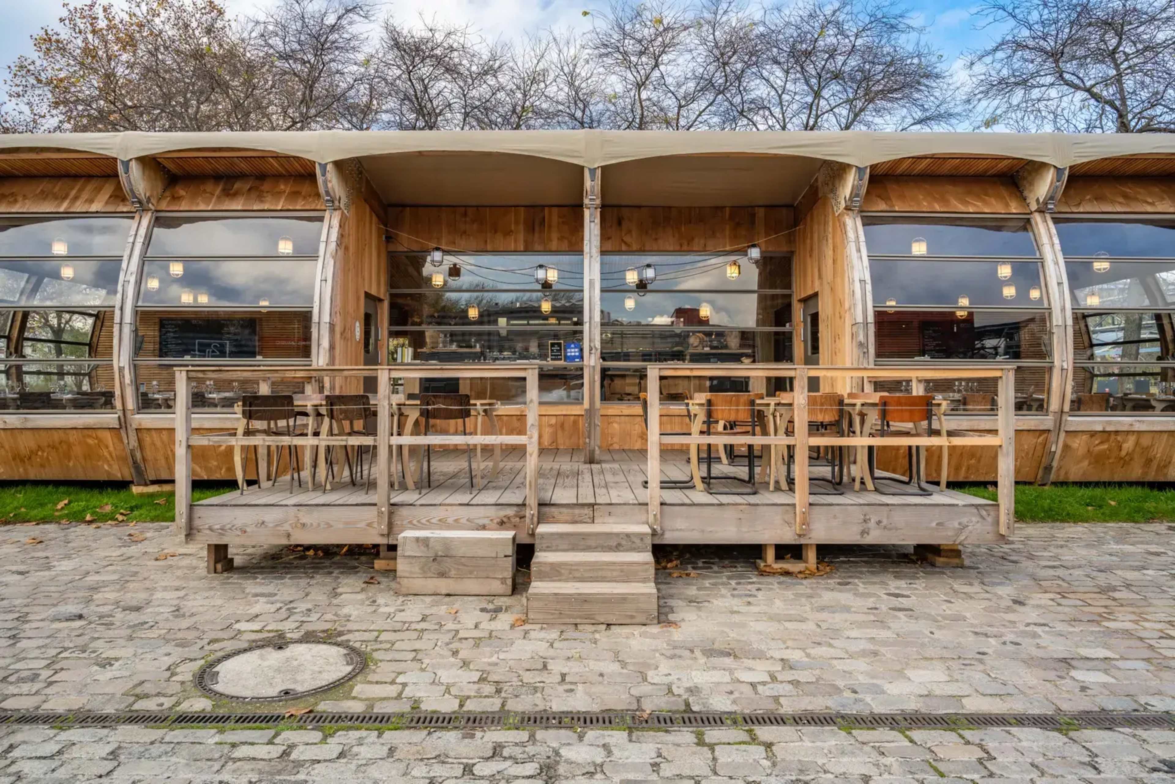 A modern wooden cafe with large glass windows and an outdoor seating area on a stone path.
