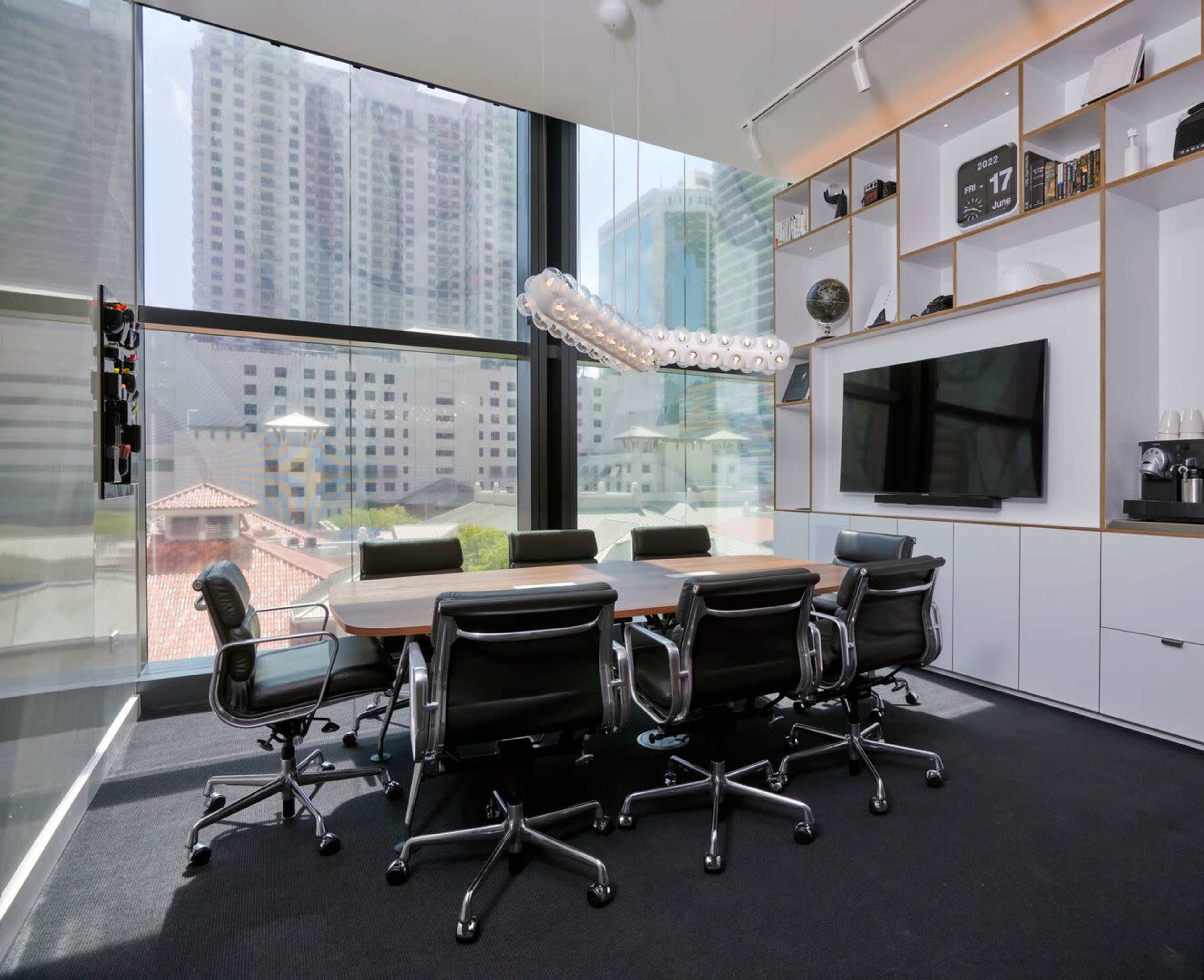 A modern conference room features a large rectangular table surrounded by ergonomic chairs, illuminated by natural light from floor-to-ceiling windows.