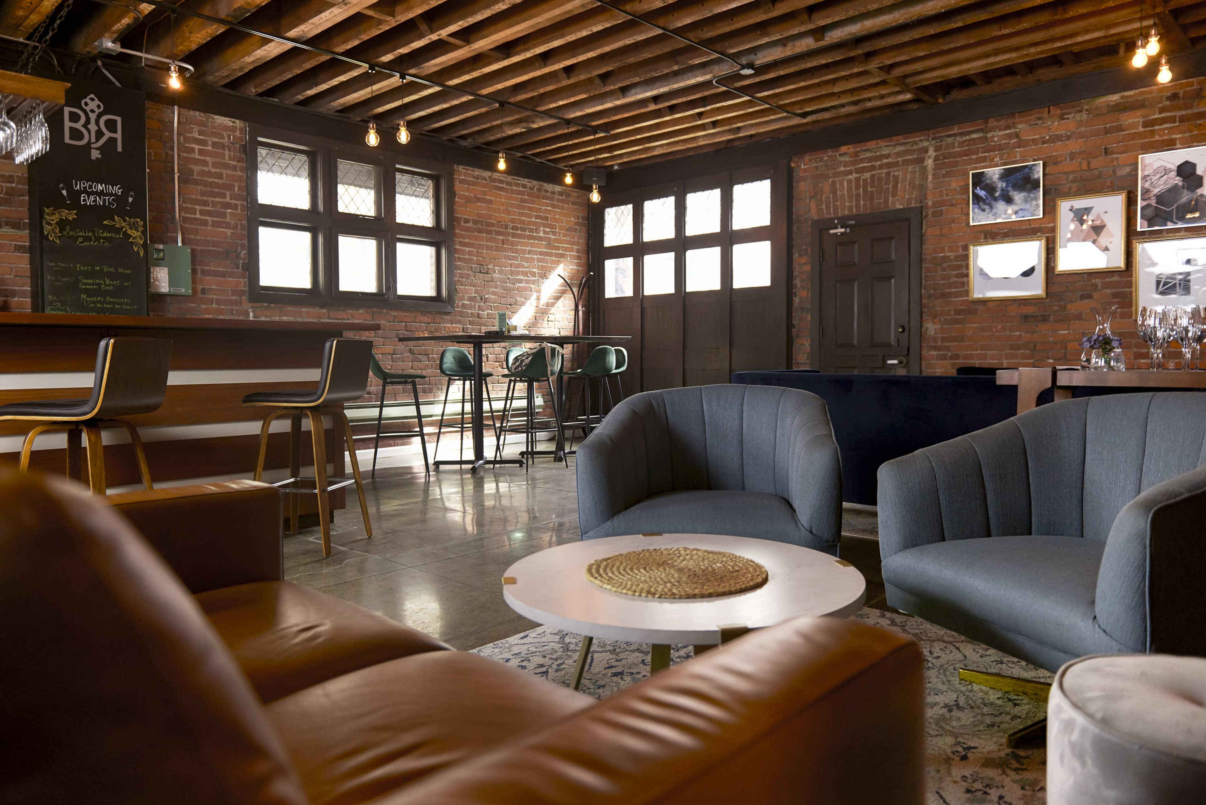 The image shows a cozy lounge area in a brick-walled space featuring modern seating, a bar, and elegant lighting fixtures.