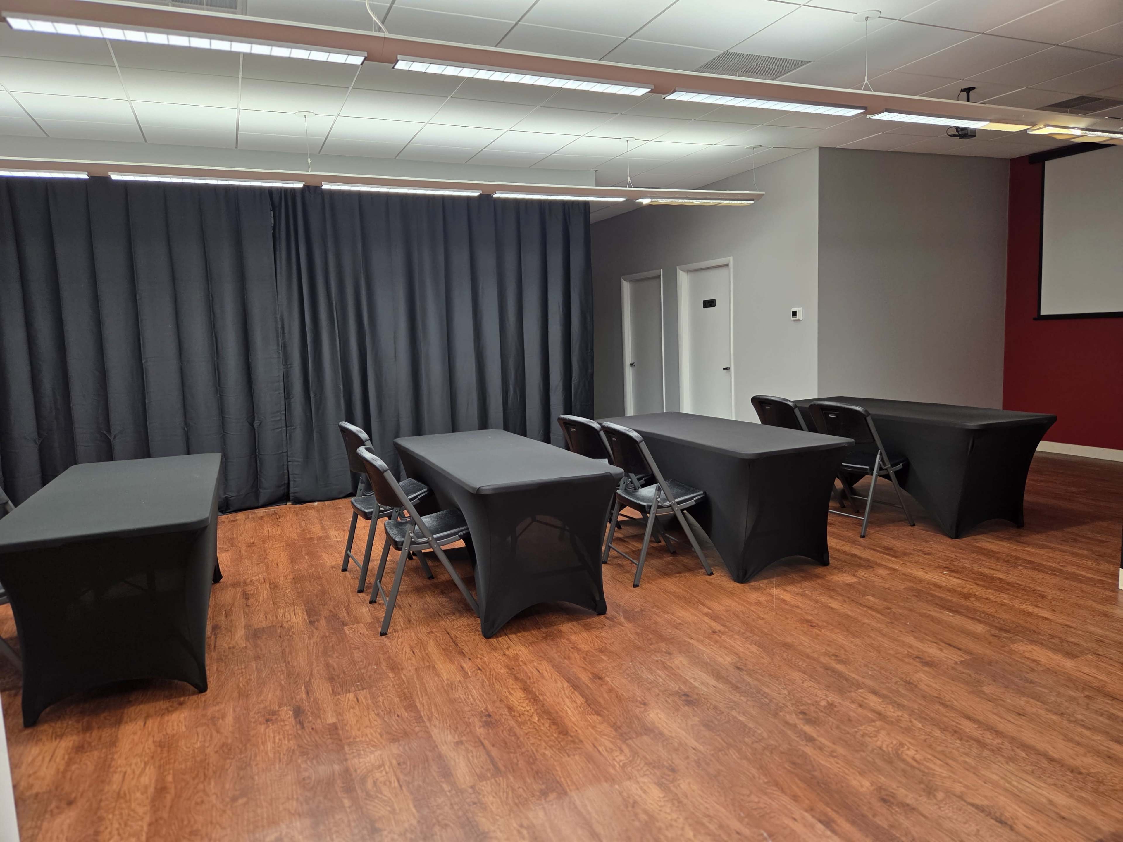 The image shows a meeting room with several tables covered in black linens and chairs arranged around them, flanked by a black curtain on one side.