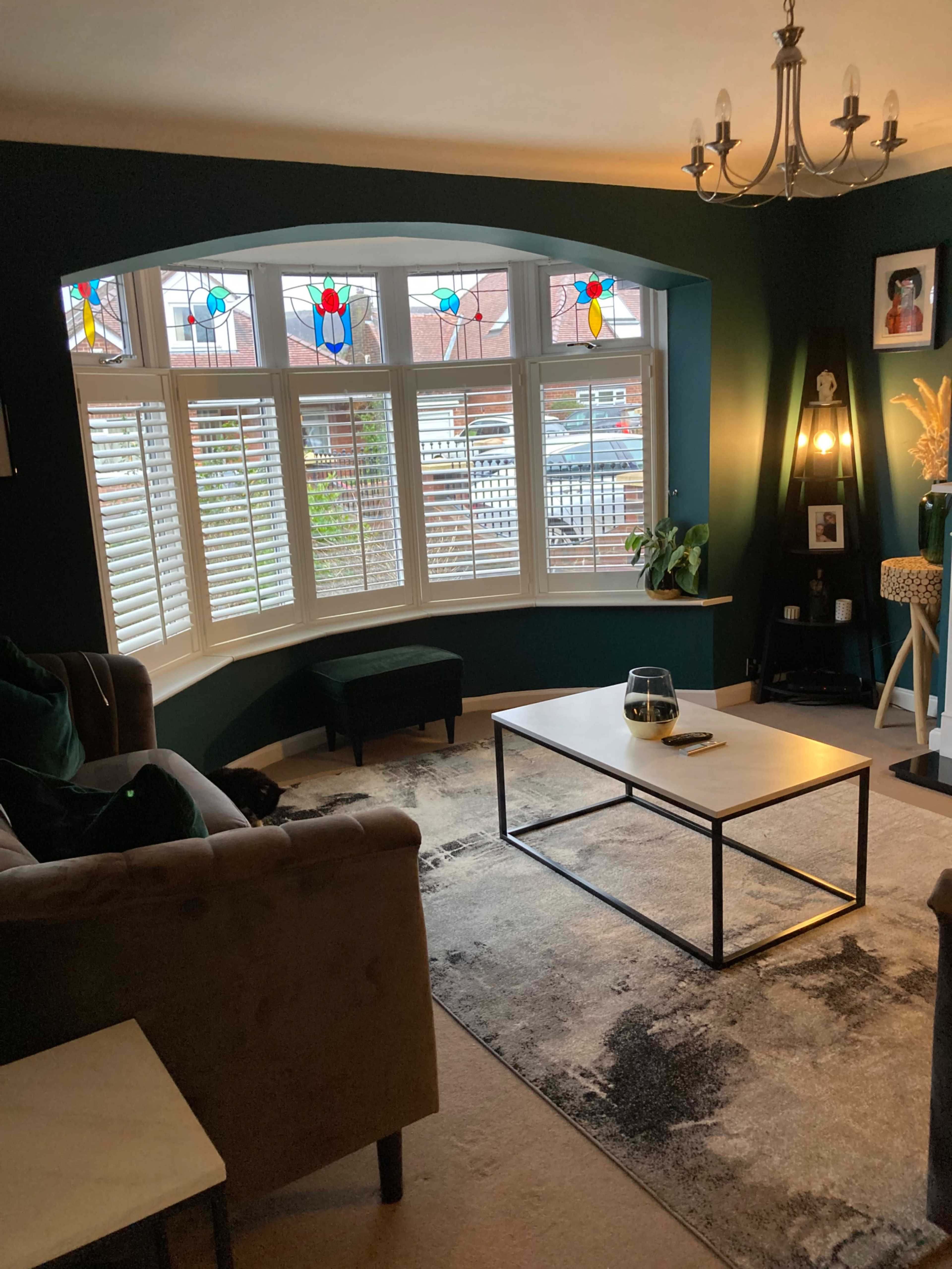 A cozy living room with a curved bay window featuring stained glass, a low coffee table, and a dark green accent wall.