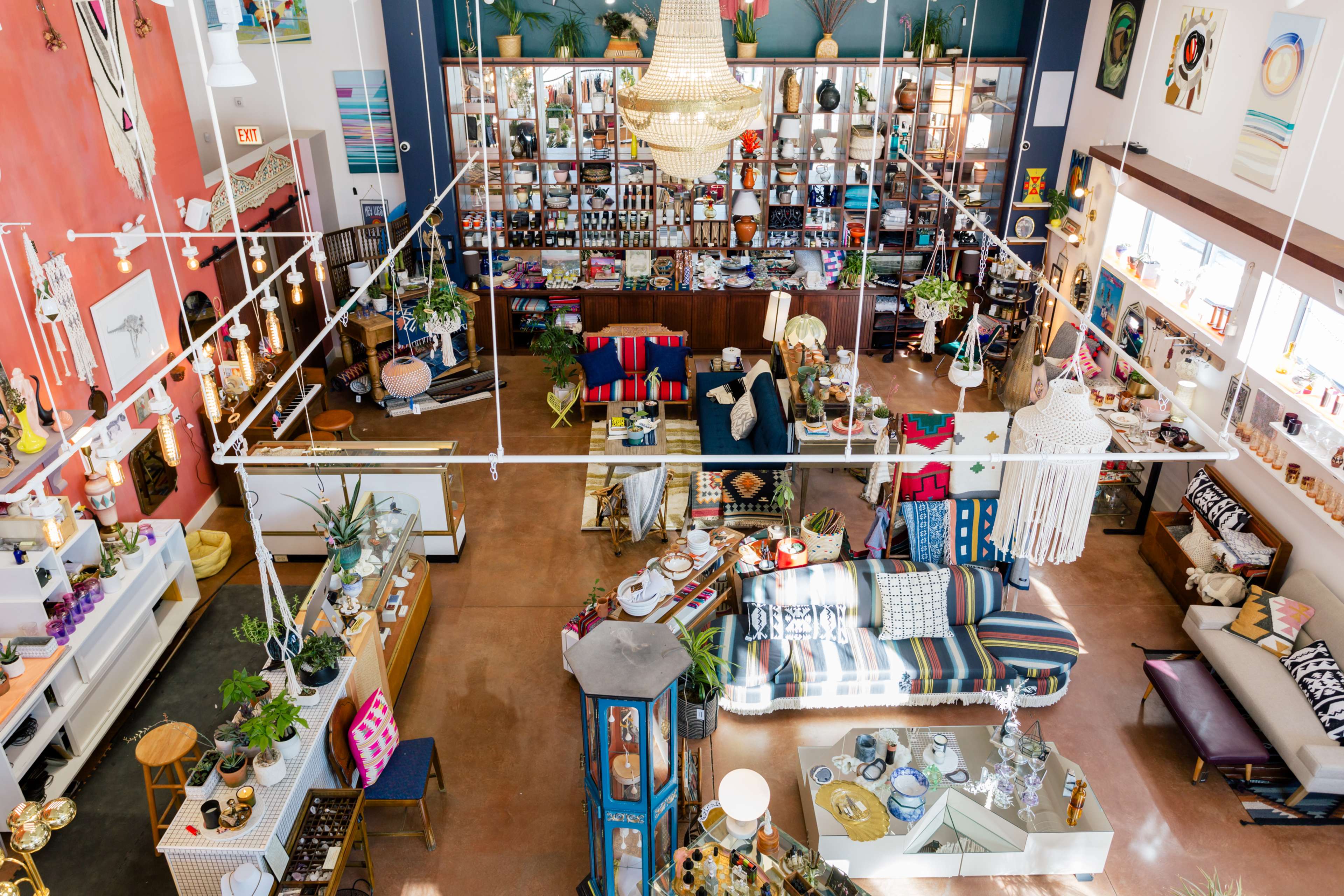 A spacious, brightly lit store interior filled with eclectic home decor items, plants, and colorful furniture arranged around distinct display areas.