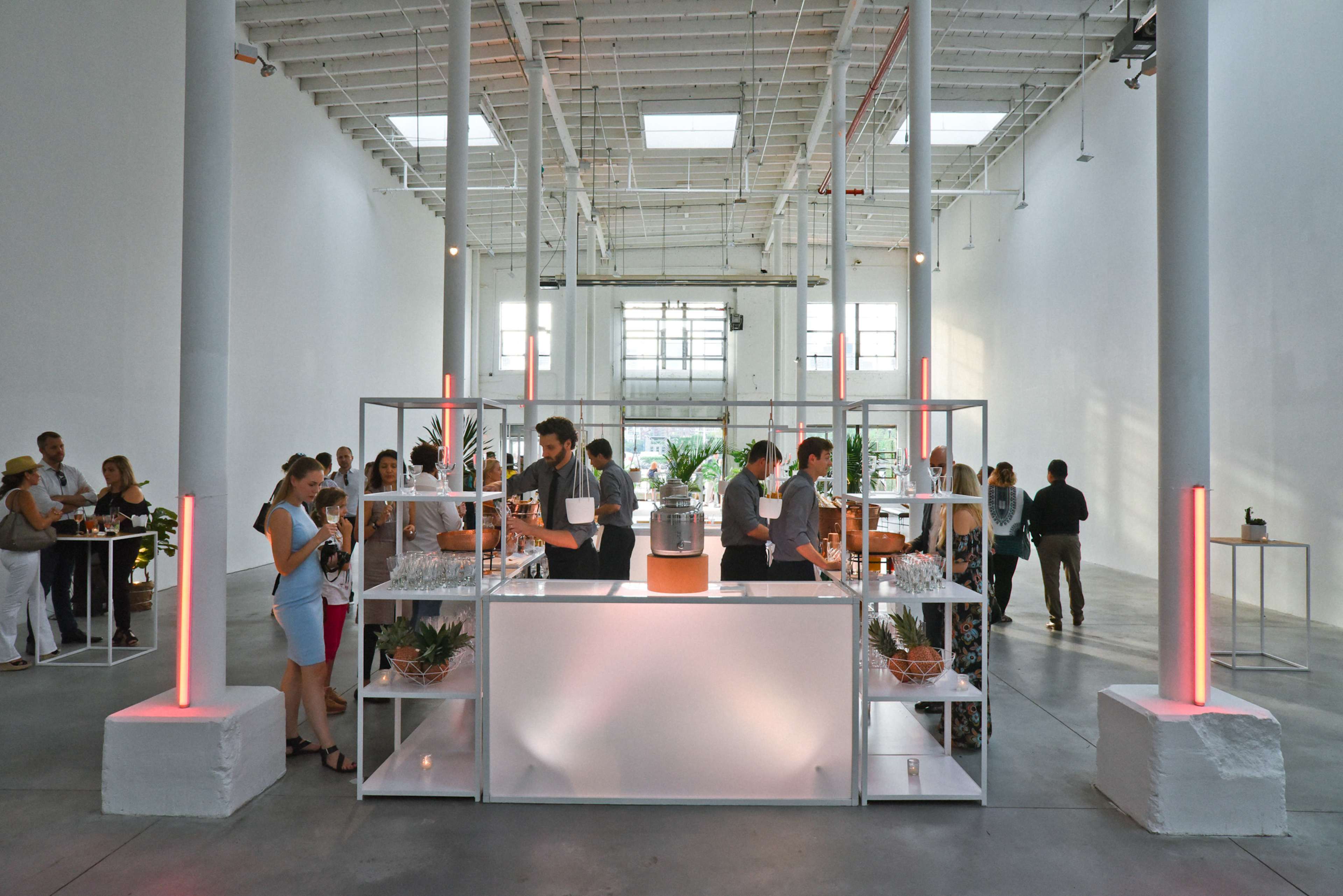 A spacious, modern venue features guests mingling around a central bar with lit displays and indoor plants.