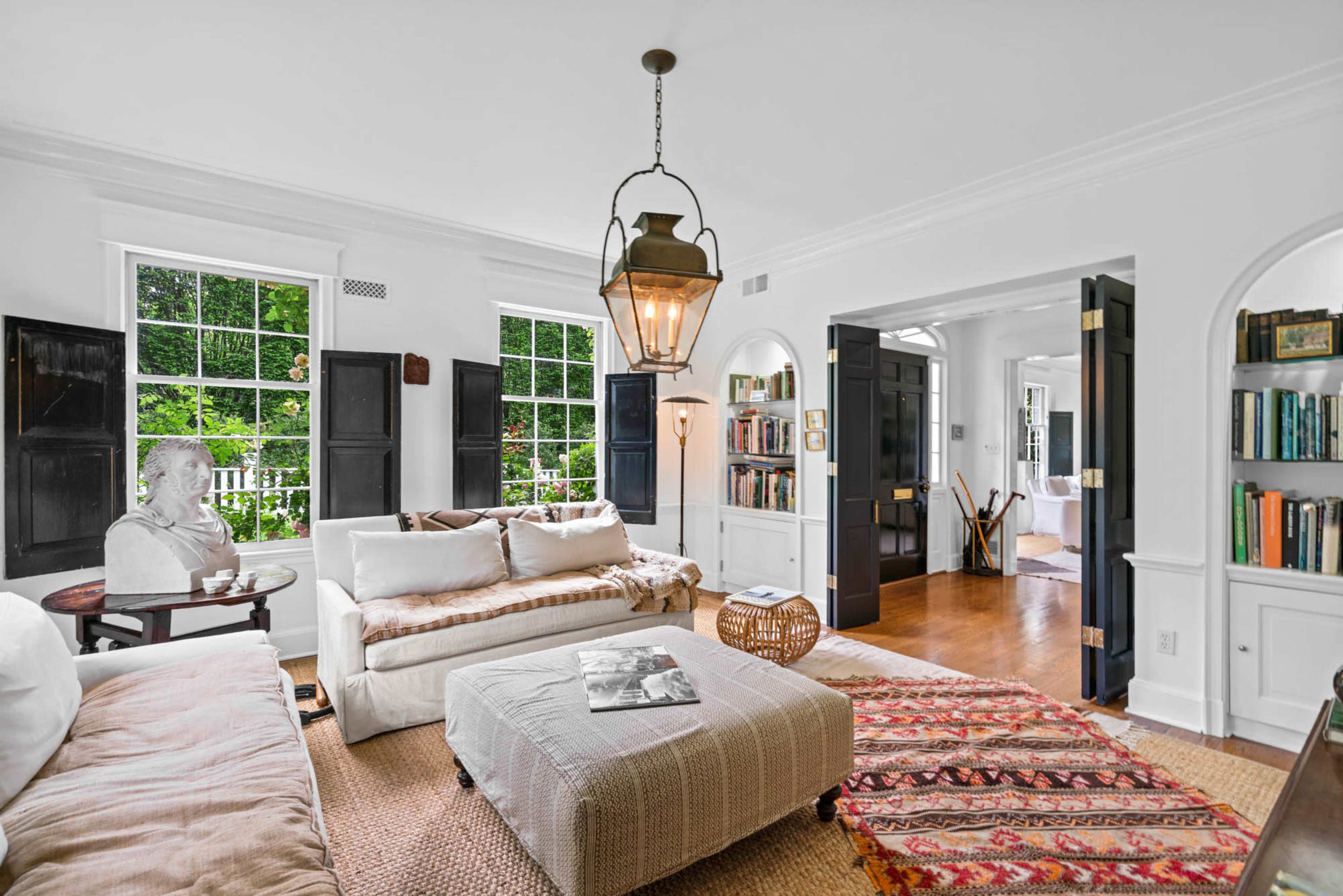 The living room features white walls, large windows, a pair of sofas, a coffee table, and a bookshelf.