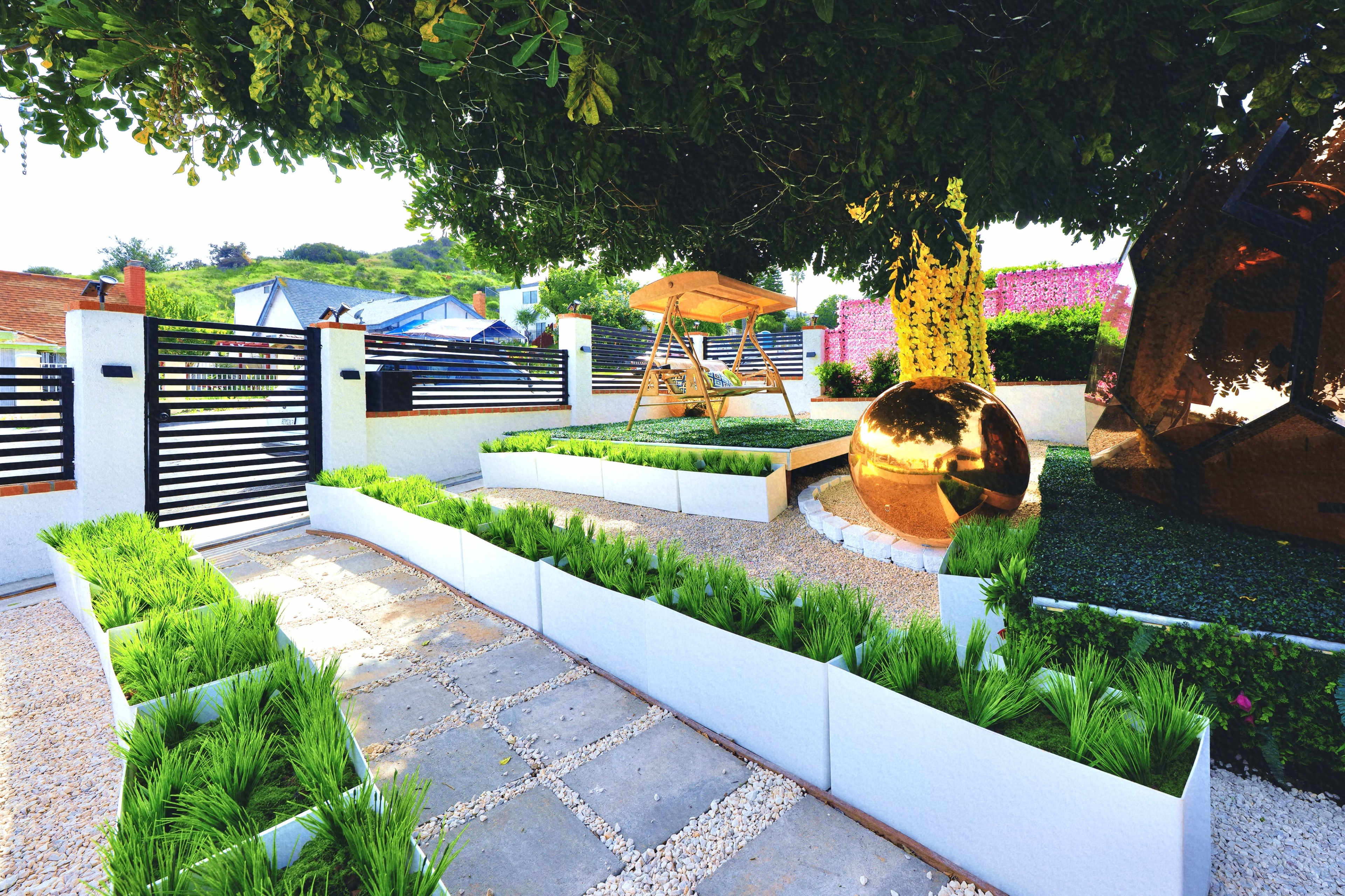 The image shows a landscaped outdoor space featuring a swing set, decorative golden orb, and neatly arranged greenery along stone pathways.