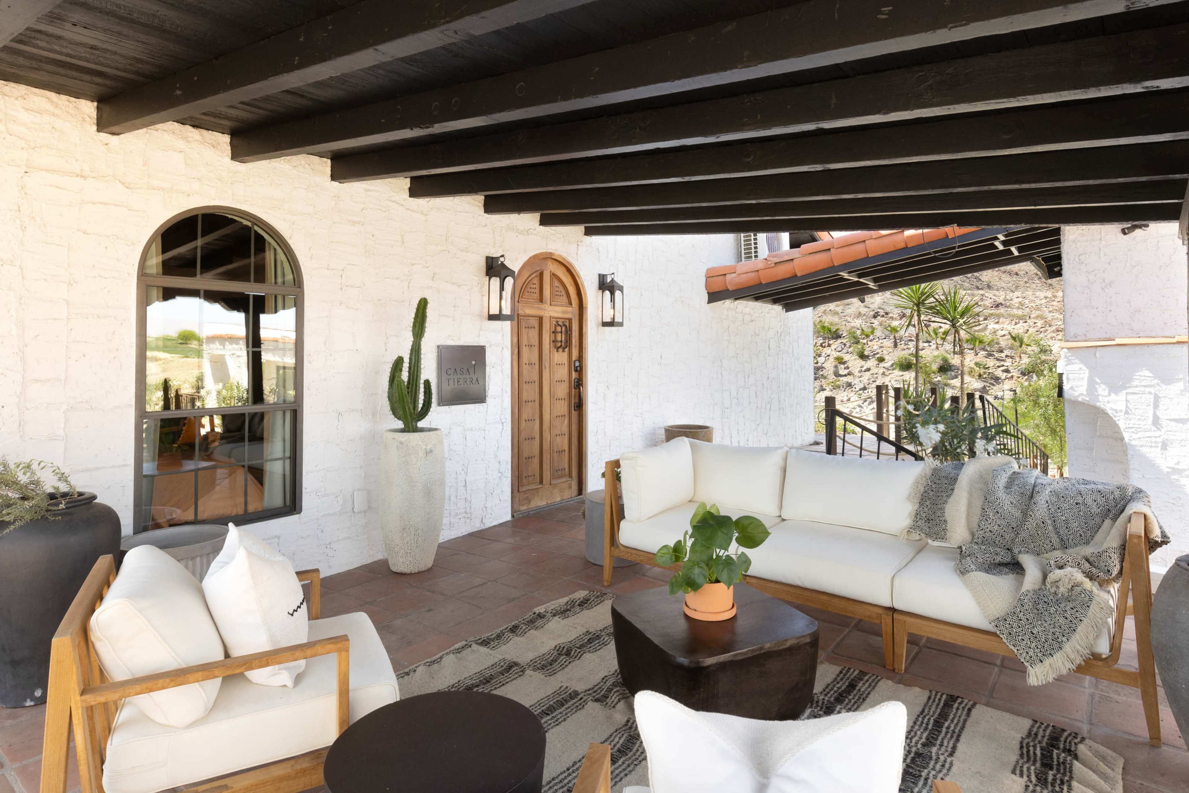 The image shows a patio area with wooden furniture, potted plants, and a stone wall.