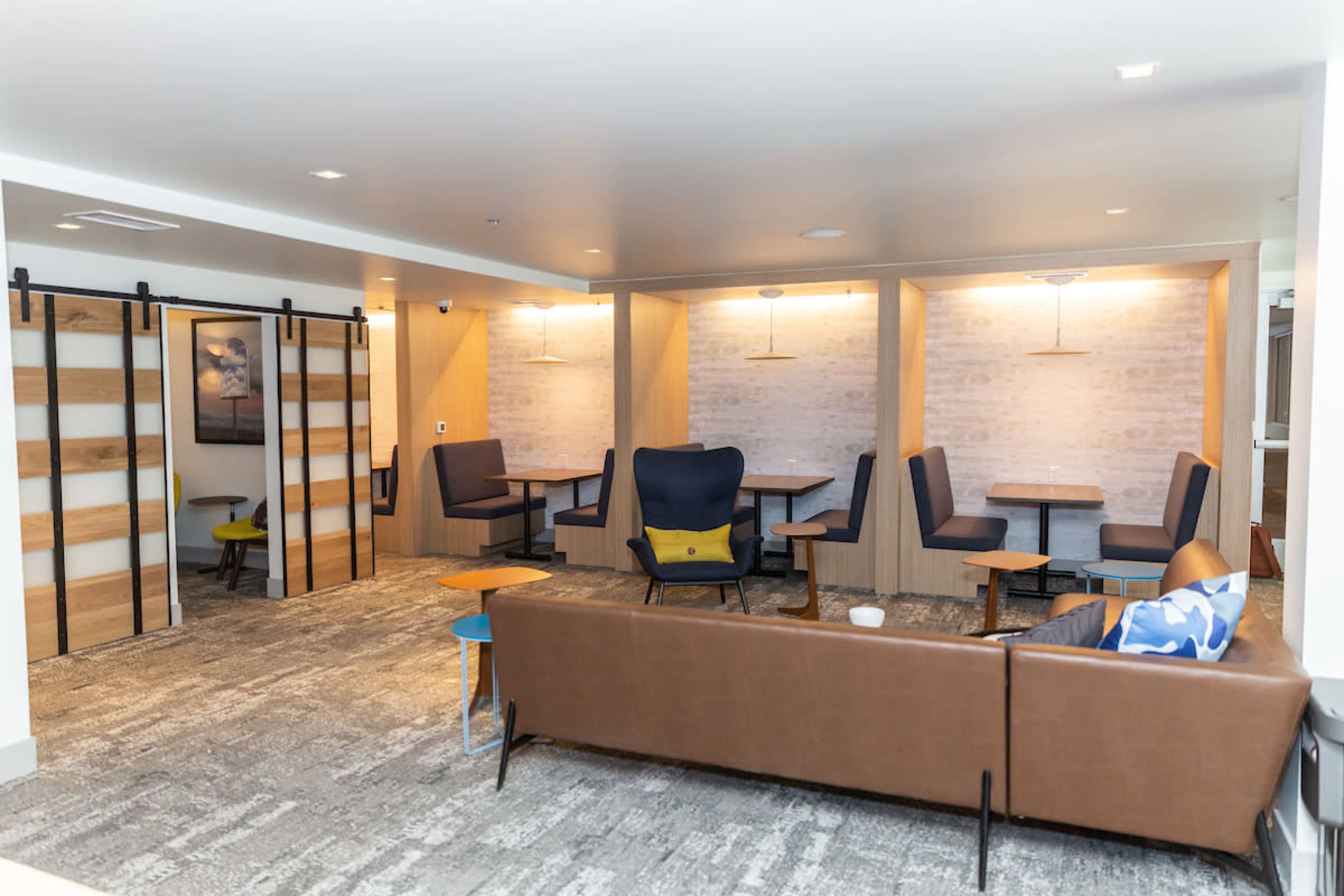 A modern lounge area with a brown sofa, small tables, and several seating arrangements against light-colored walls with wood accents.
