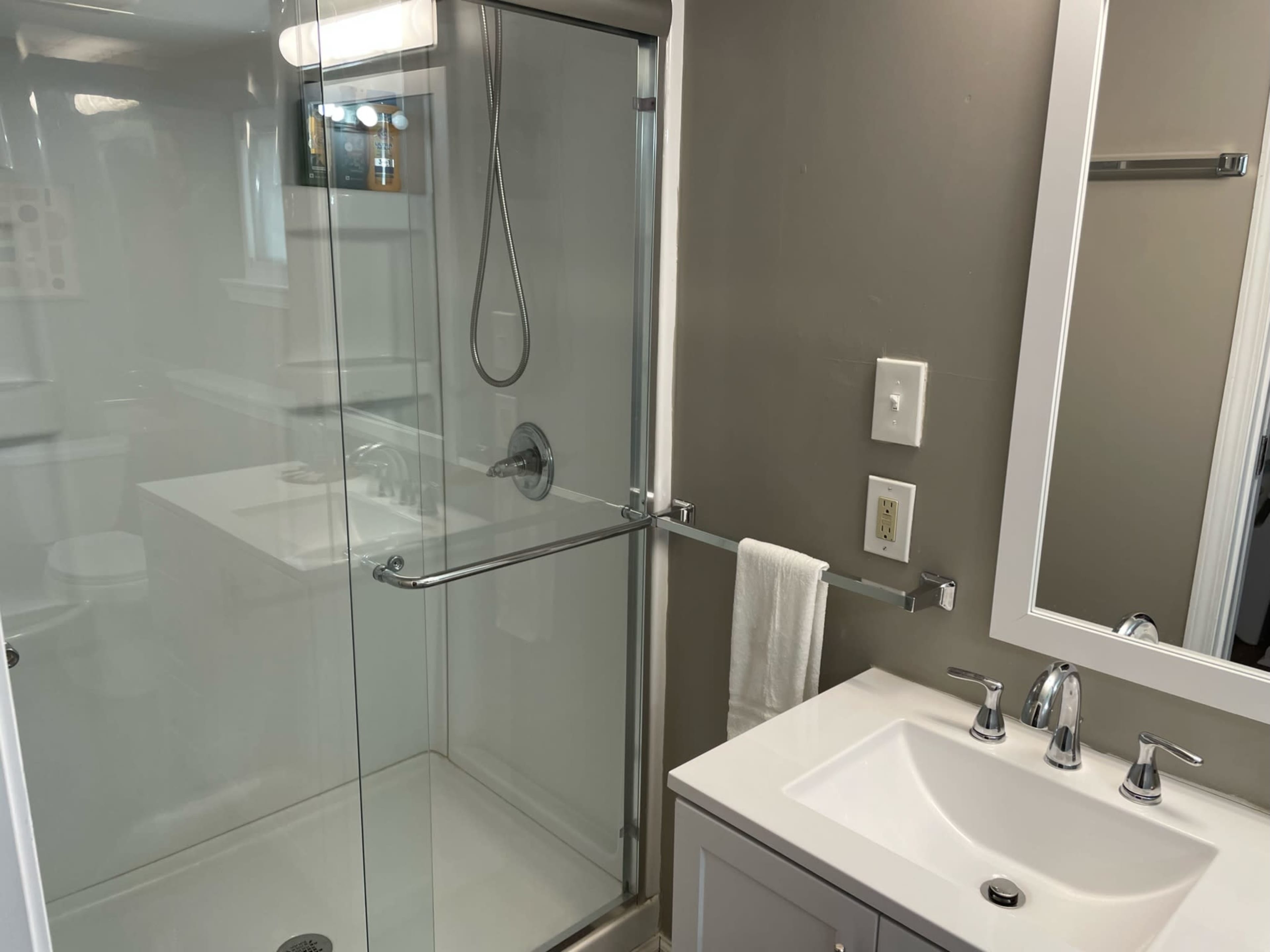 A modern bathroom featuring a frameless glass shower, a sink with a white countertop, and light-colored walls.