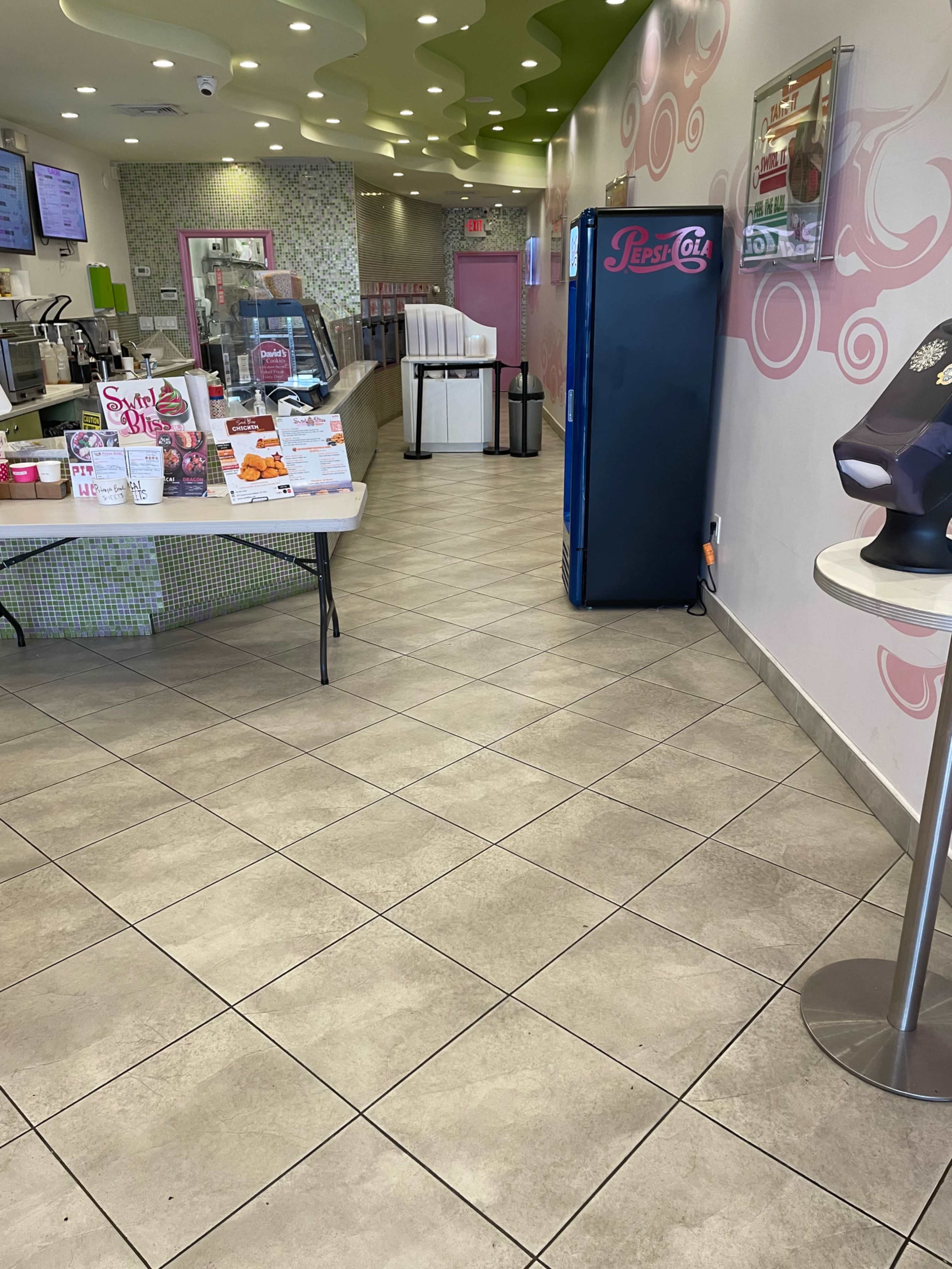 The interior of an ice cream shop with a counter, tables, and a soda vending machine.