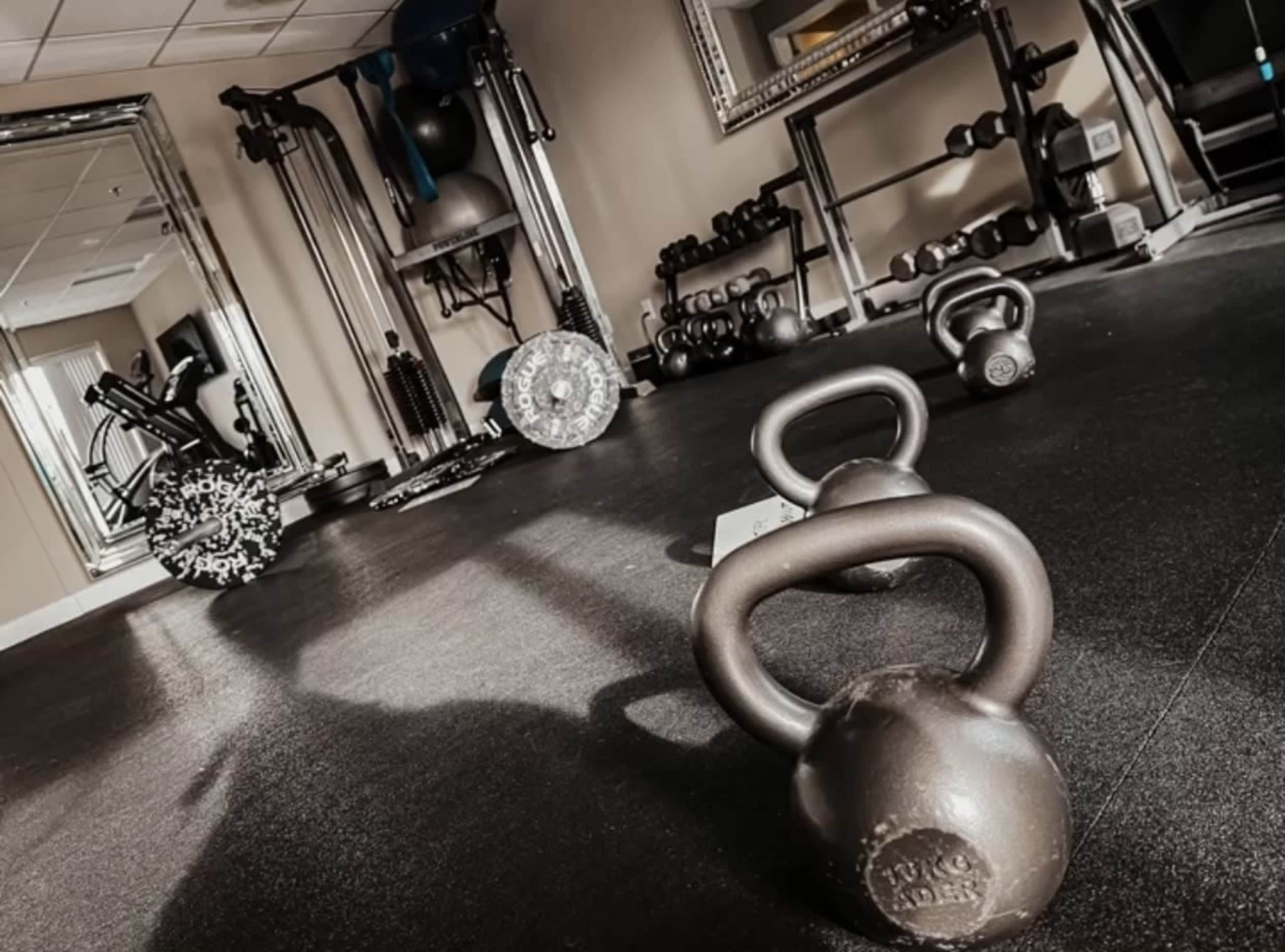 The image shows a gym interior with kettlebells on the floor, various exercise equipment, and a mirror reflecting the space.
