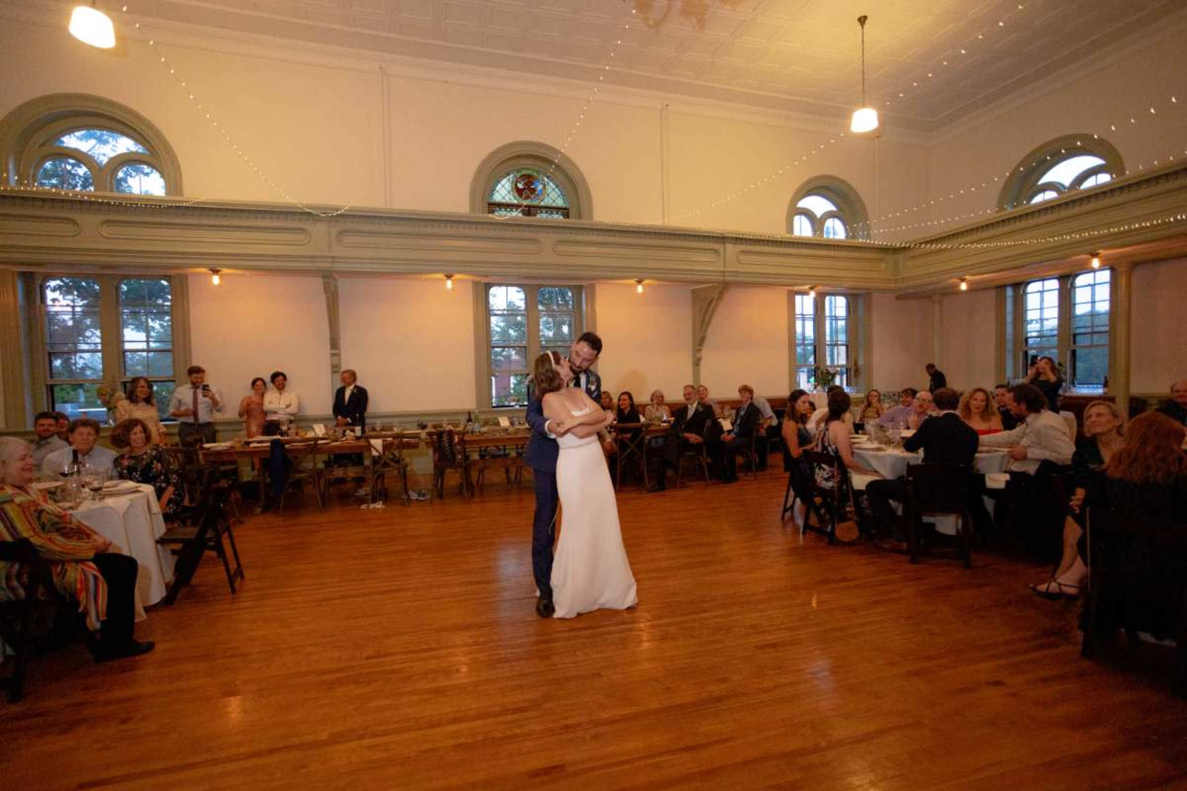 A couple is dancing in the center of a beautifully decorated reception hall filled with guests seated at tables.