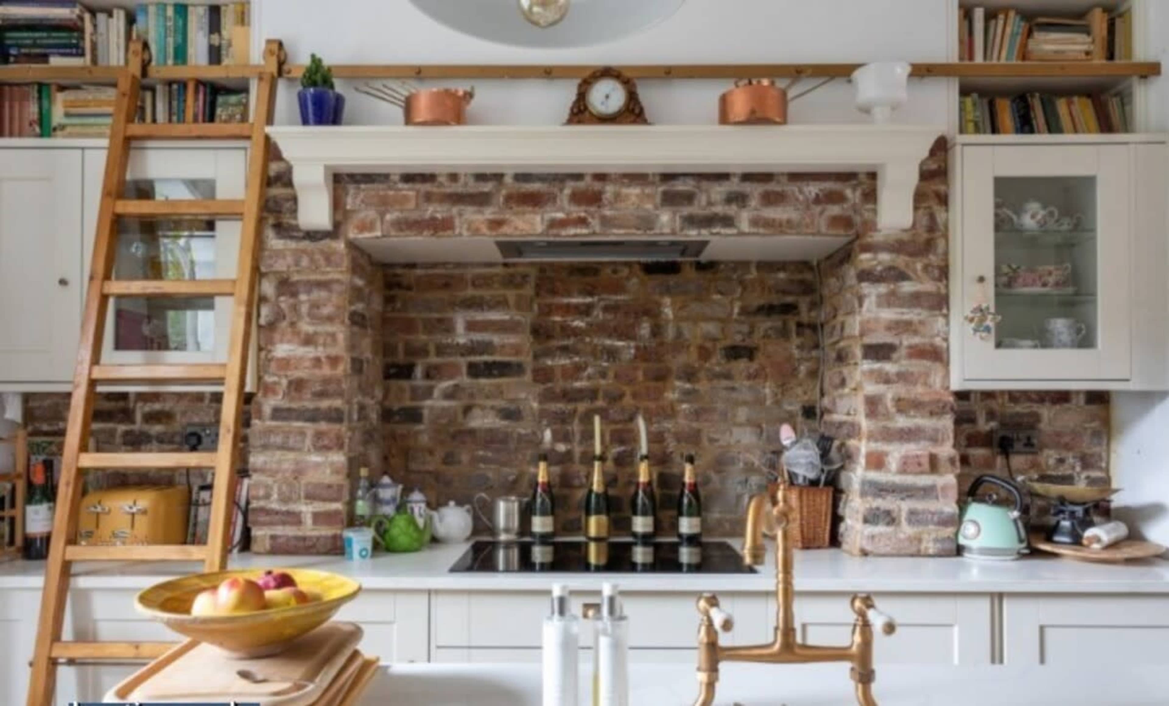 A kitchen with a brick feature wall, a stove, and a wooden ladder leaning against the cabinets.
