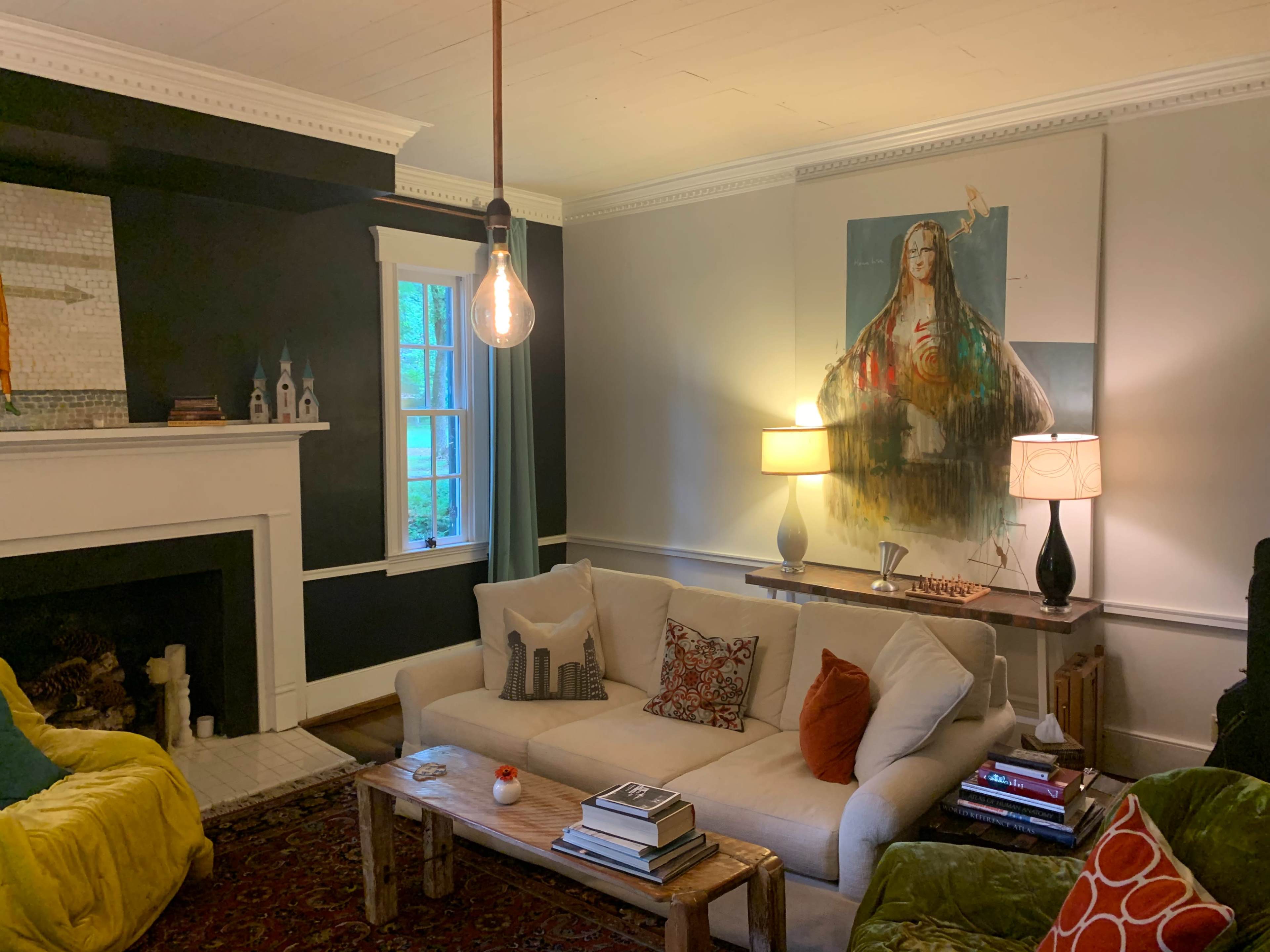 The image shows a living room with a sofa, two lamps, a wooden coffee table, and a large painting on the wall above it.