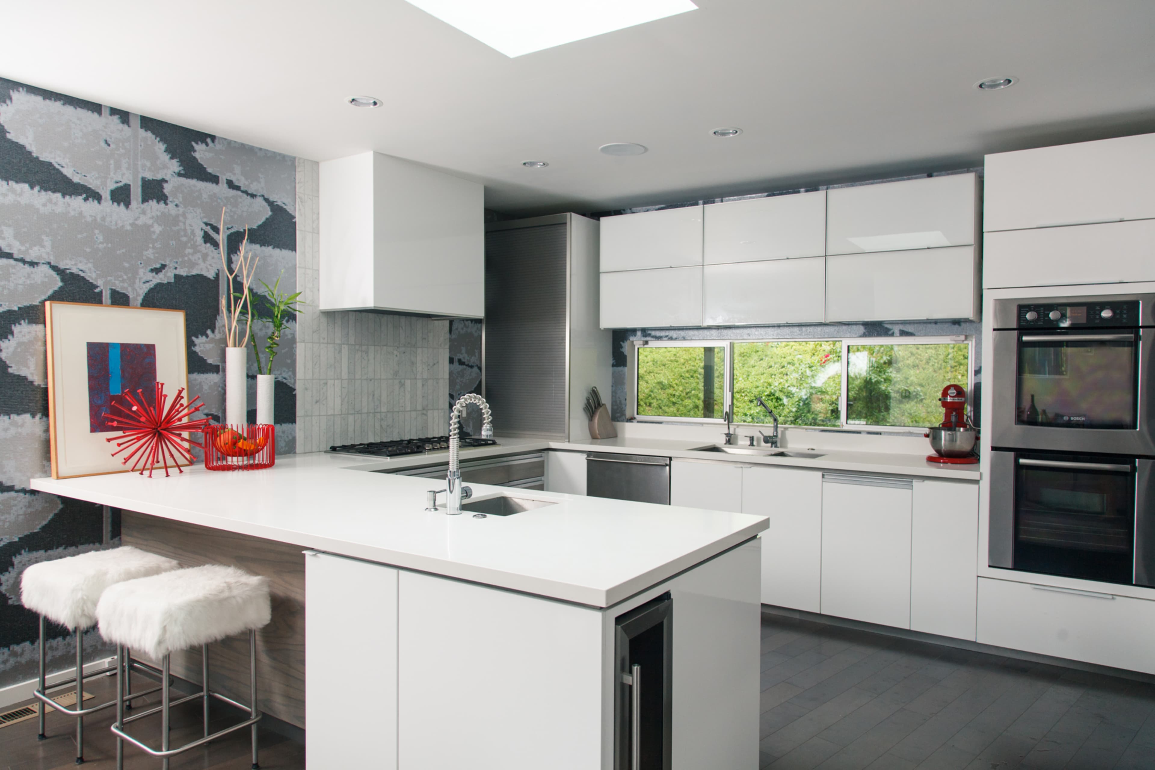 The kitchen features white cabinetry, a large island with seating, and a window that overlooks greenery.