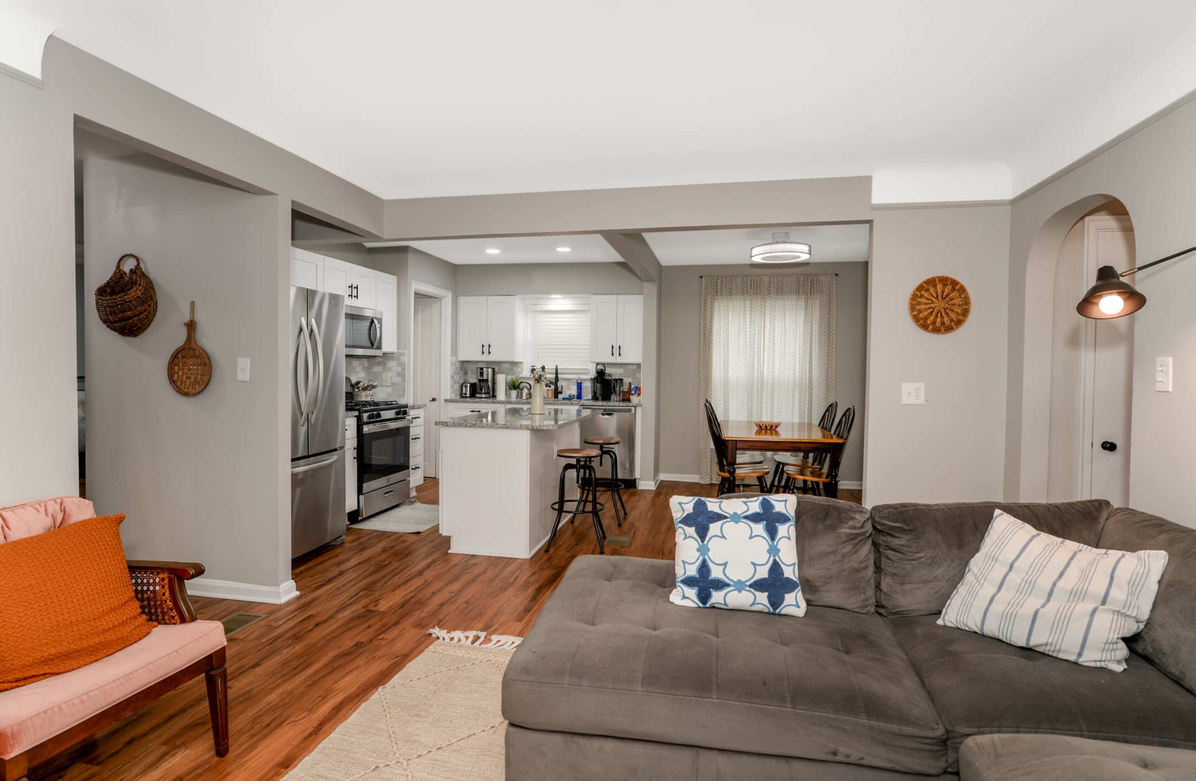 A cozy living room features a sectional sofa, a small dining area with a table and chairs, and a well-equipped kitchen visible in the background.