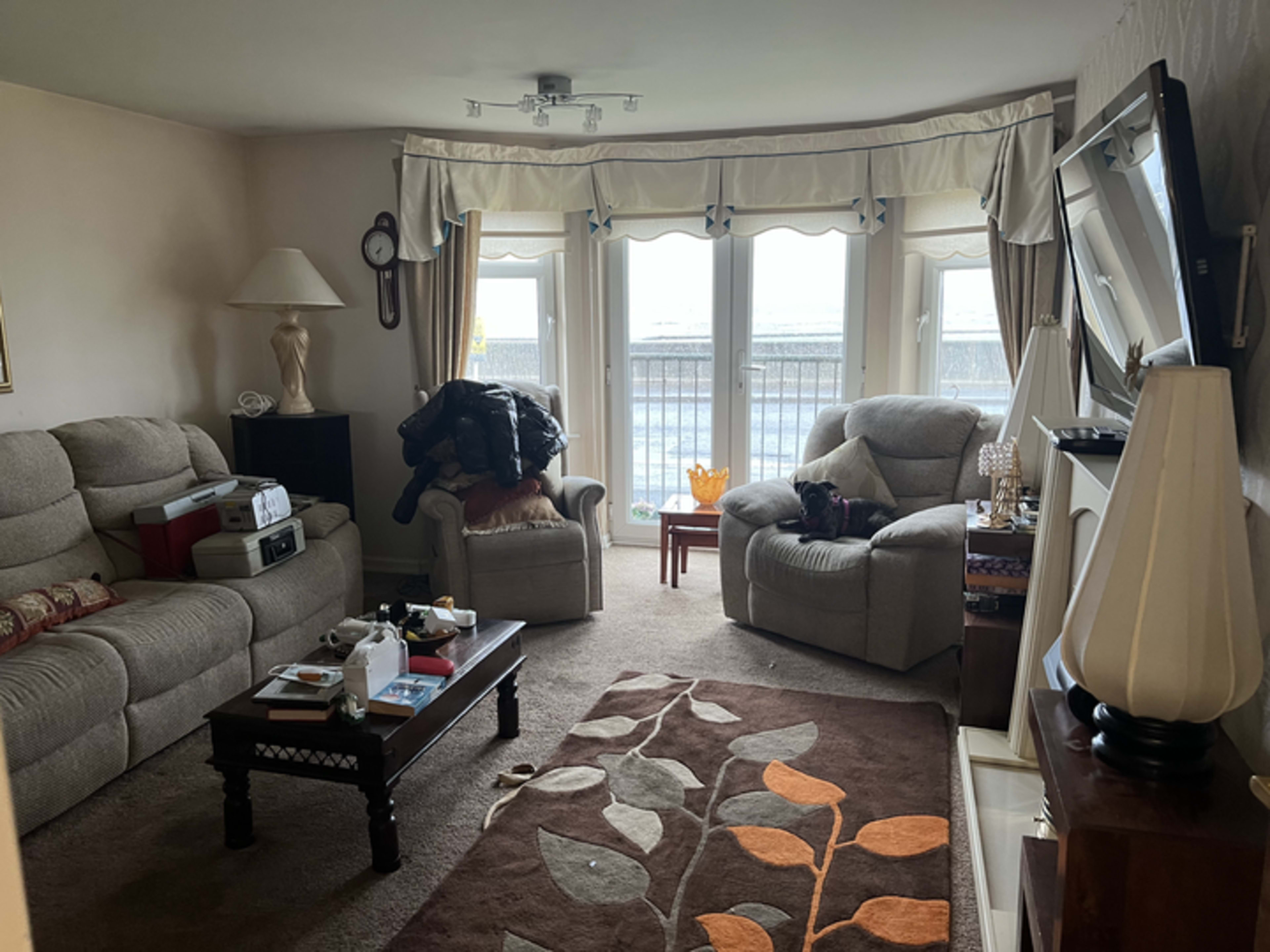 The living room features two beige sofas, a wooden coffee table, and large windows with a view, illuminating the space with natural light.