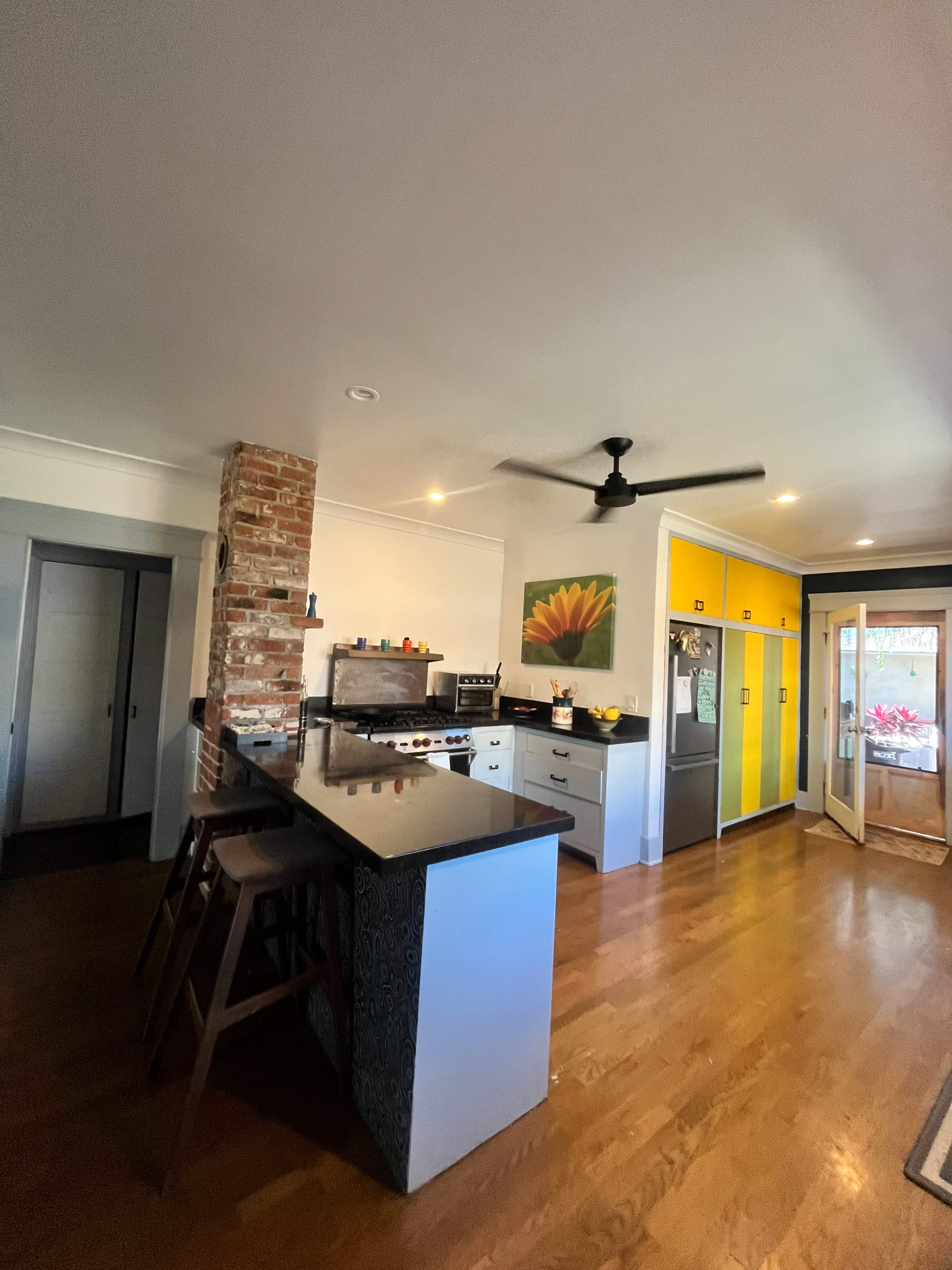 The image shows a modern kitchen featuring a brick wall, yellow cabinets, stainless steel appliances, and a wood floor.