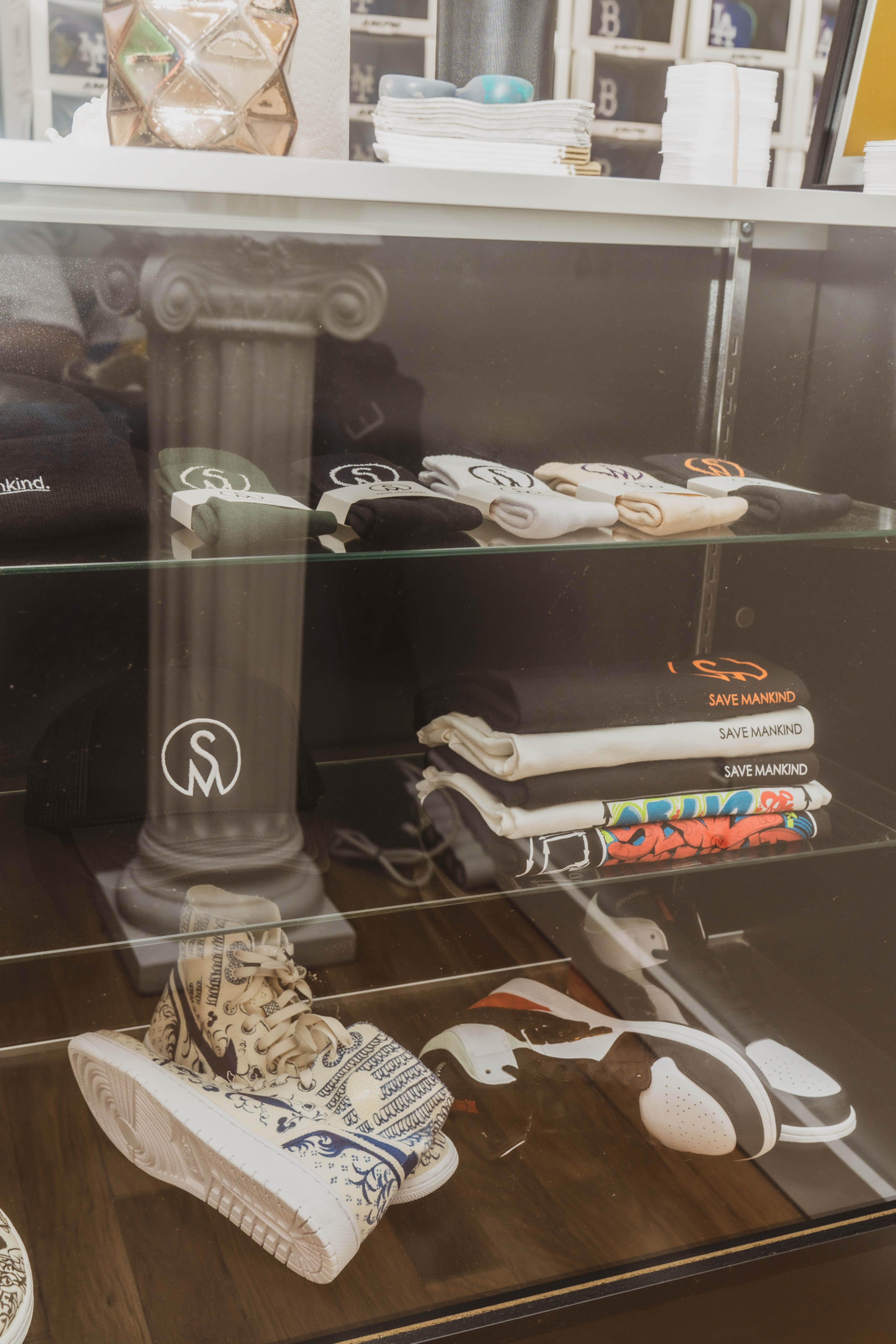 A display case showcases a selection of folded shirts and sneakers, along with a hat, featuring brand logos and various designs.