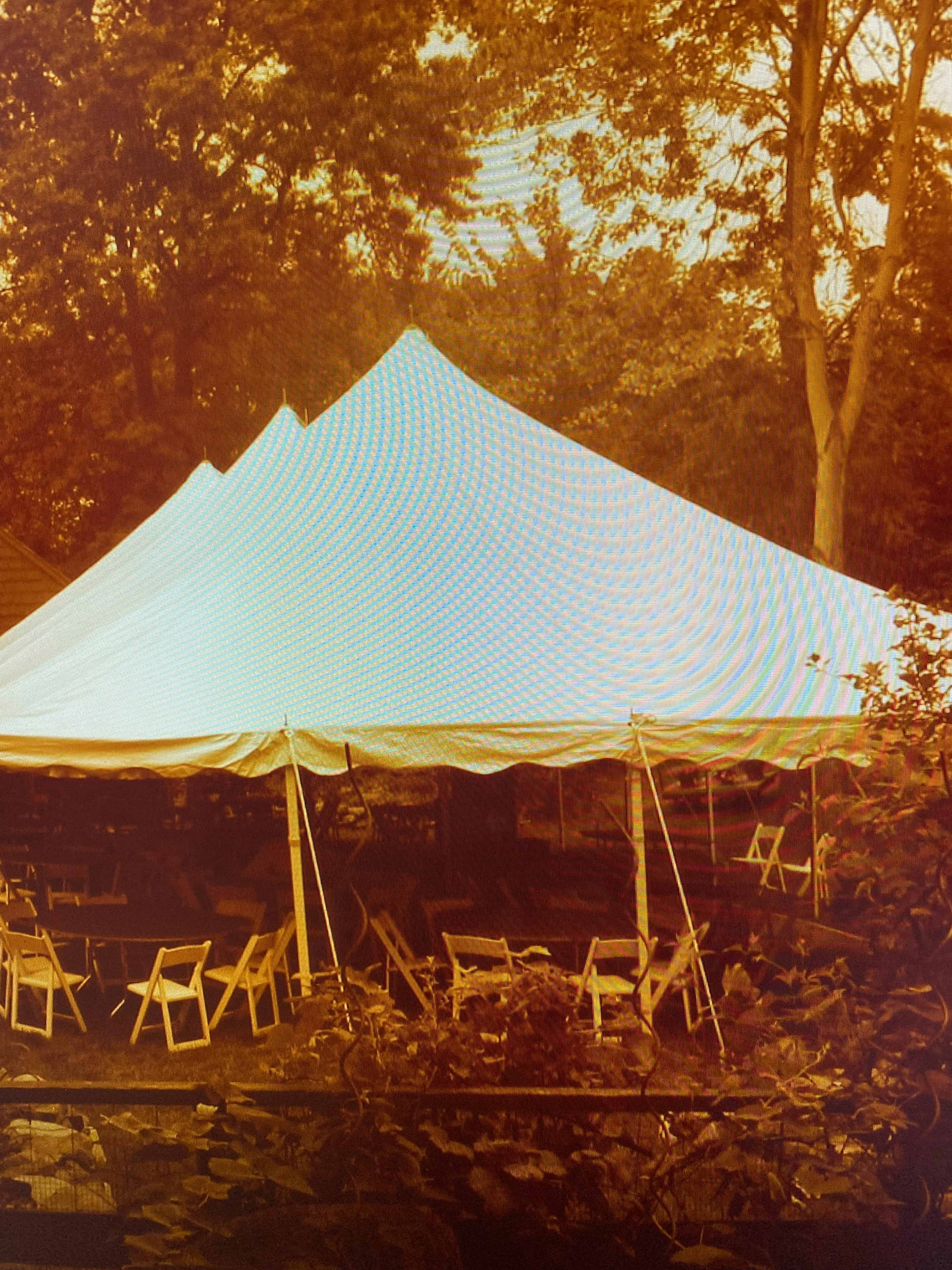 A large white tent is set up in a wooded area, surrounded by empty chairs.