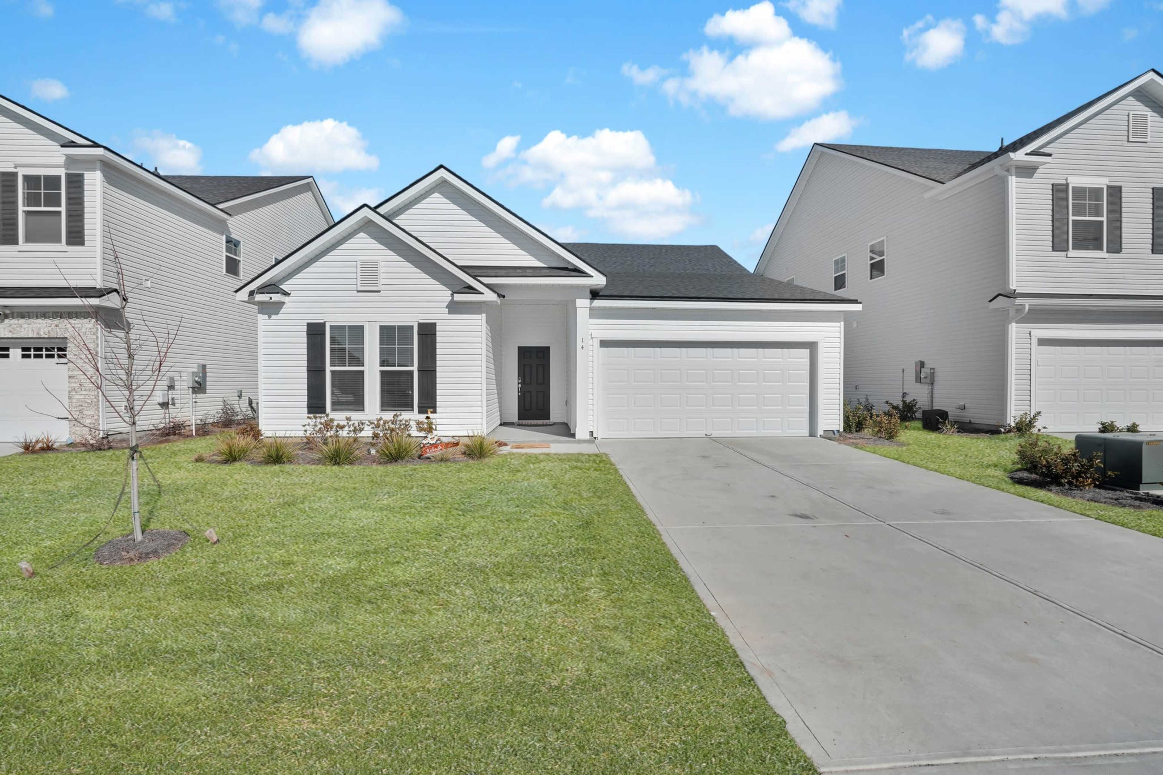 A single-story house with a light-colored exterior and a two-car garage sits on a neatly landscaped yard with green grass.