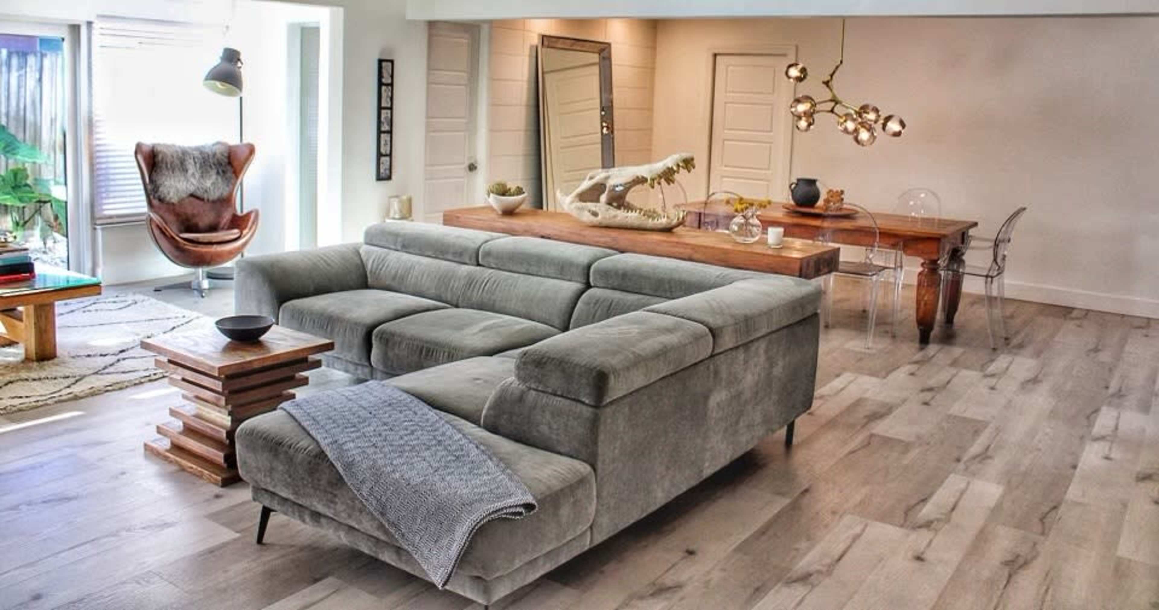A modern living space with a grey sectional sofa, a wooden dining table, and a decorative light fixture overhead.